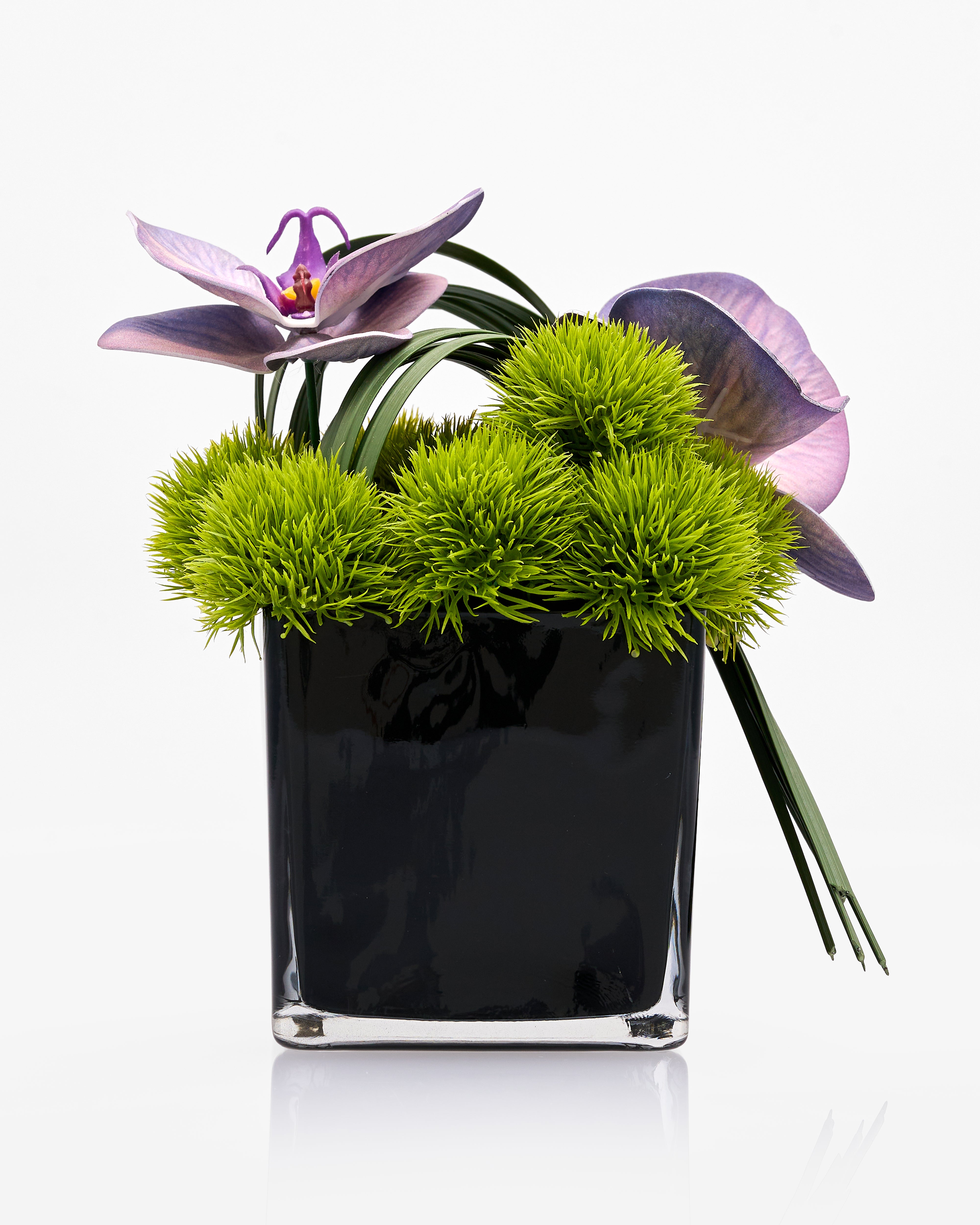 Artificial Flowering plant with violet blooming flower and green bush leaves in a black crystal glass vase