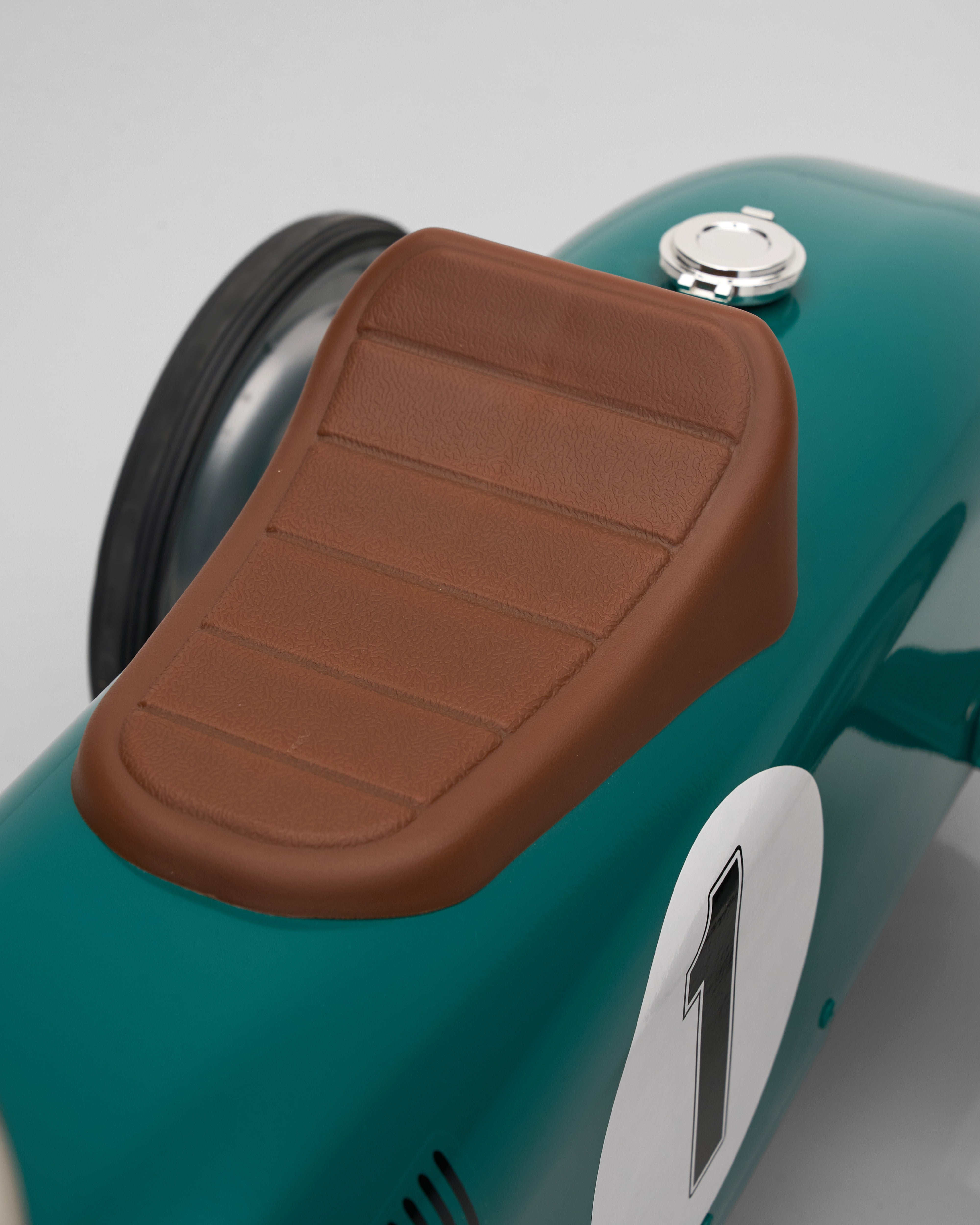 Close-up of a brown seat on a teal scooter with a number 1 on a light gray background