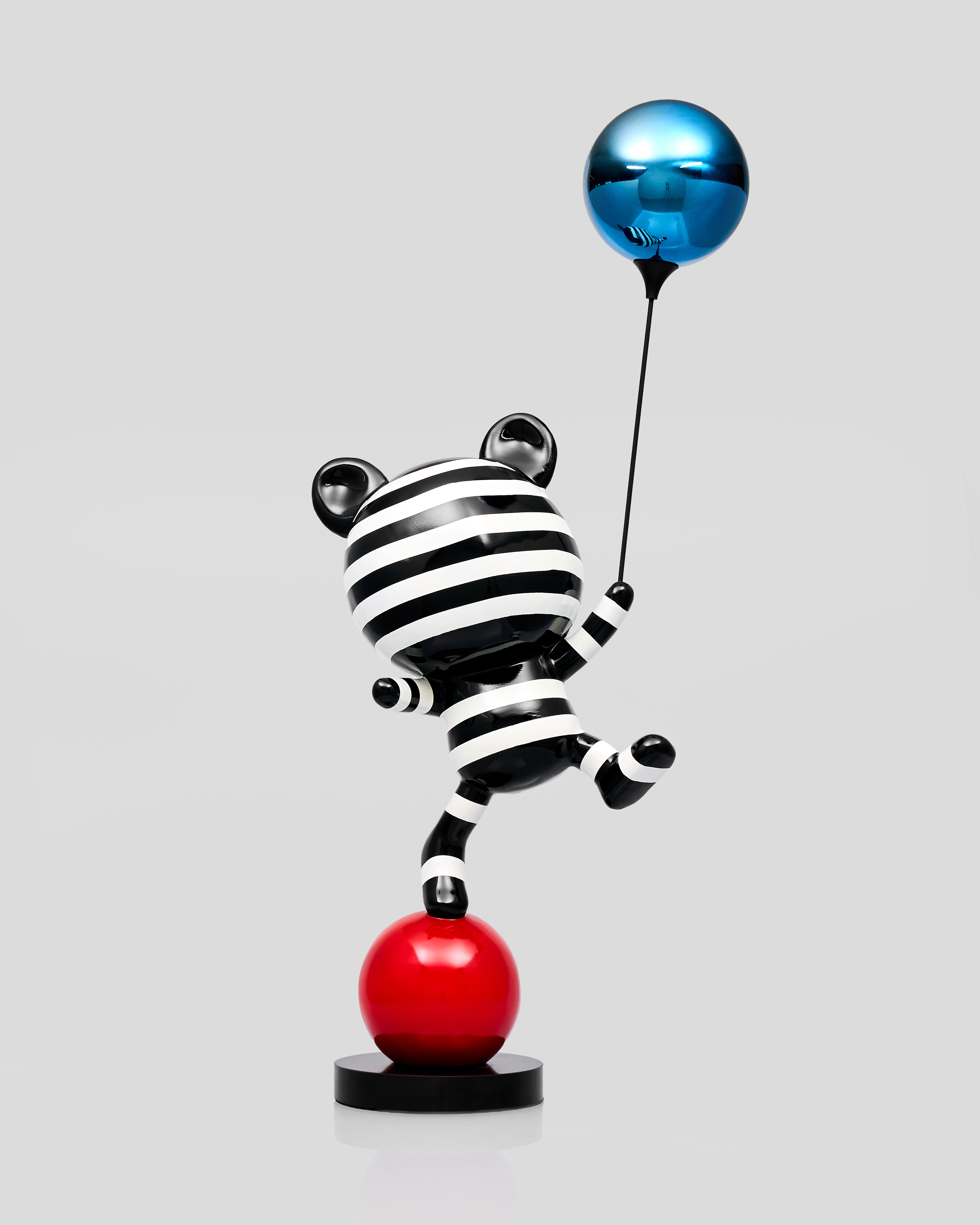 Black and white striped cat figurine with a blue balloon on a red ball against a gray background