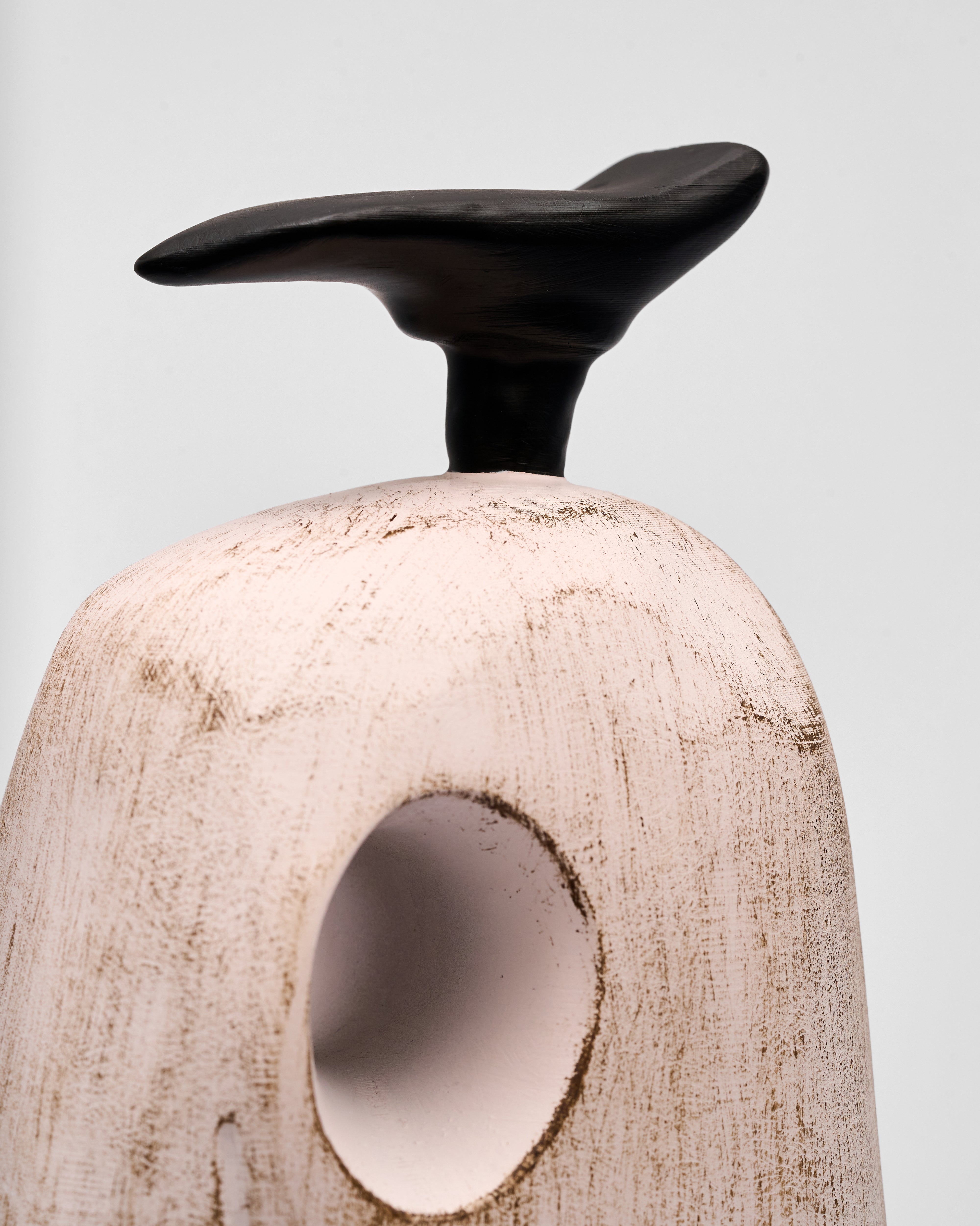 wooden sculpture with black top and textured beige base on a light gray background