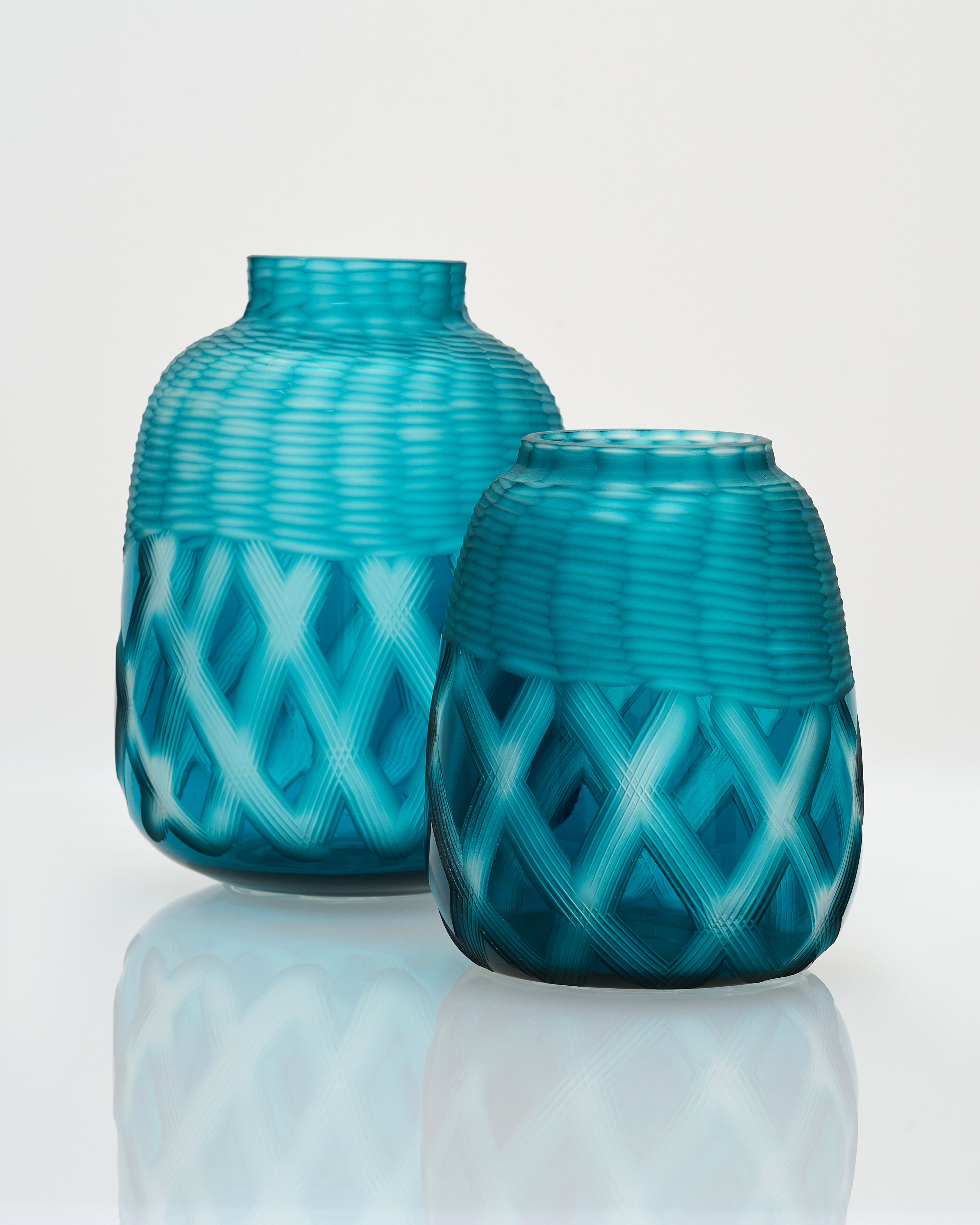 Two turquoise glass vases with woven pattern on a white background