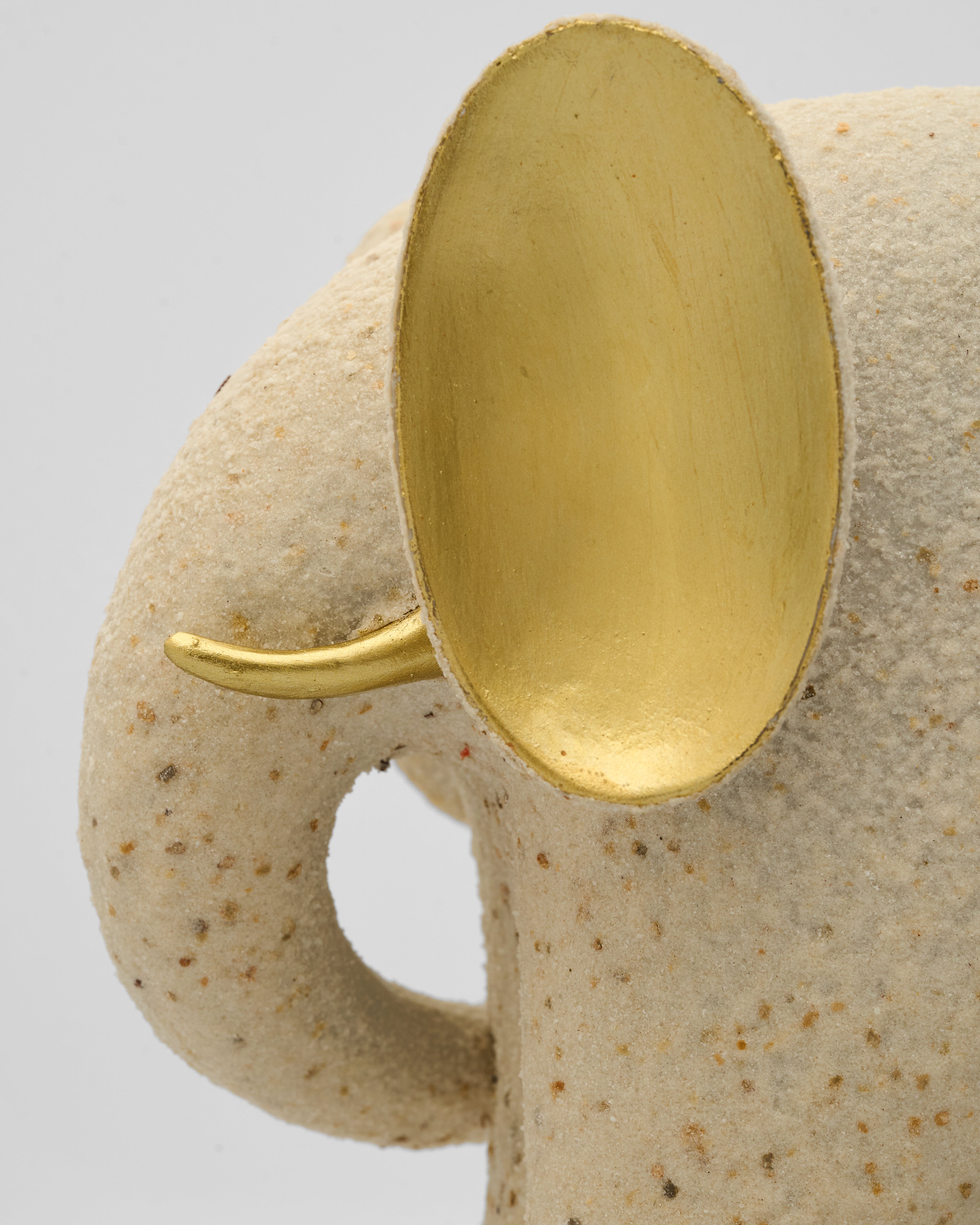 Close-up of a ceramic elephant figurine with a gold trunk on a light gray background