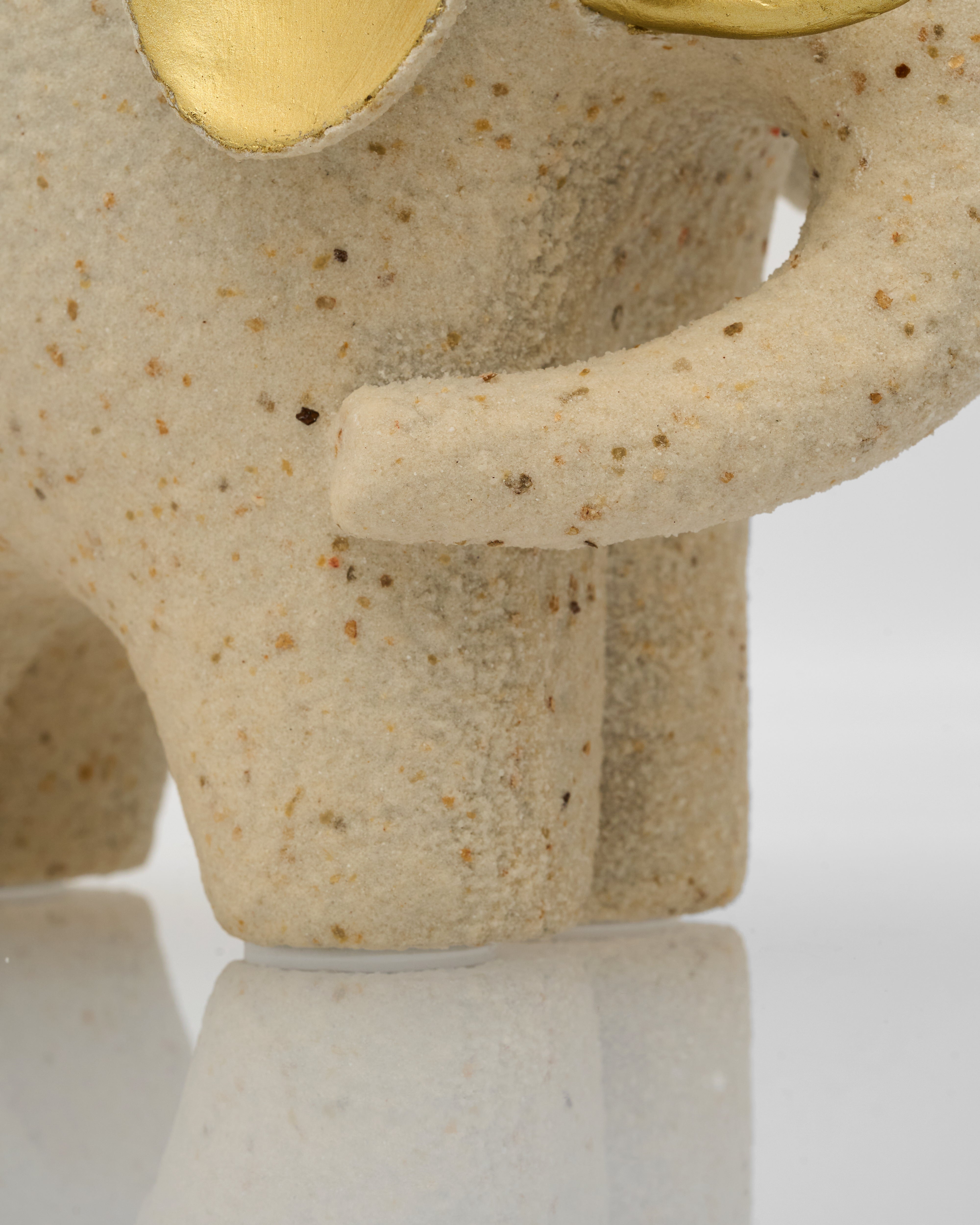 Close-up of a beige ceramic sculpture with gold accents on a white background