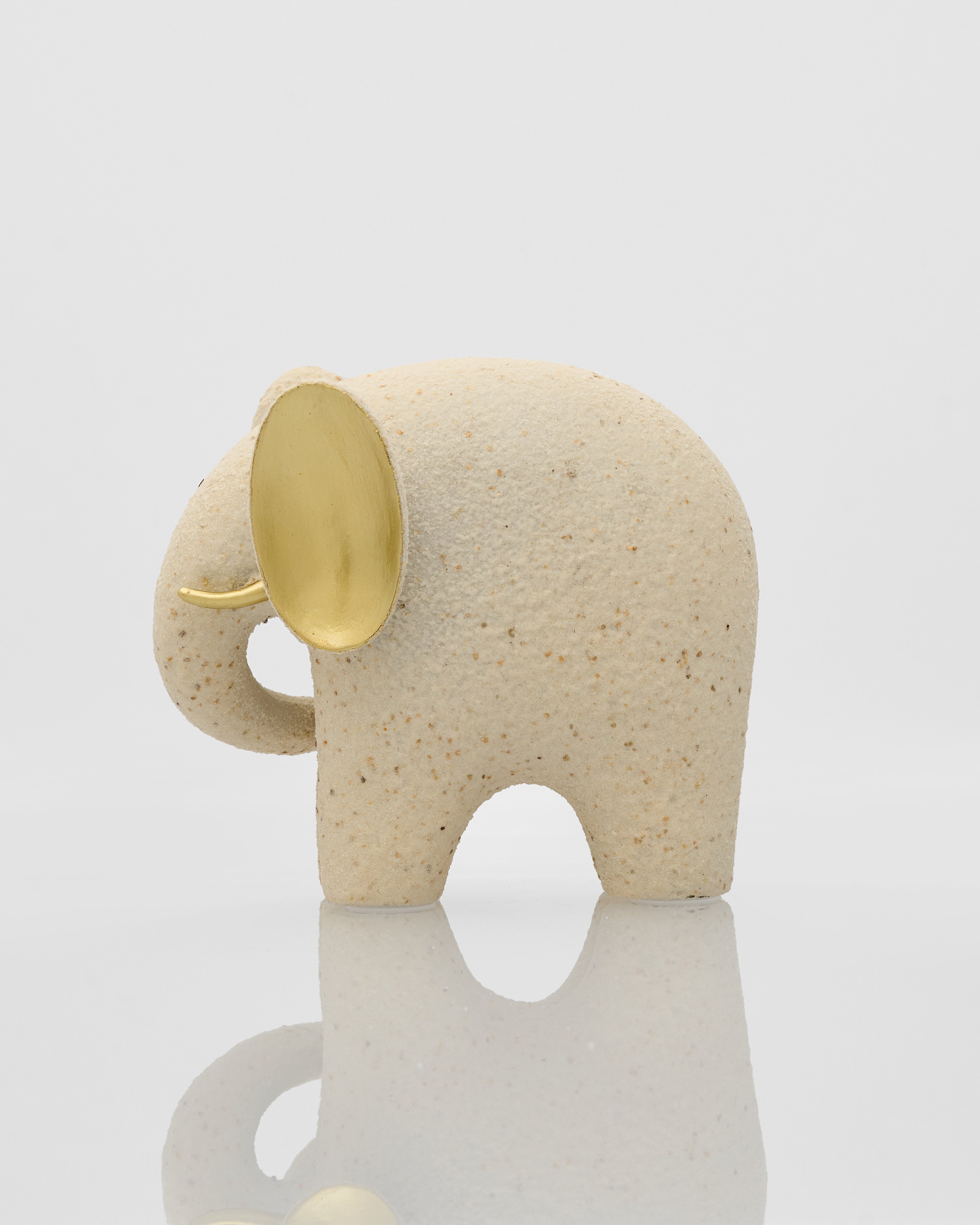Beige elephant figurine with a gold ear on a reflective surface