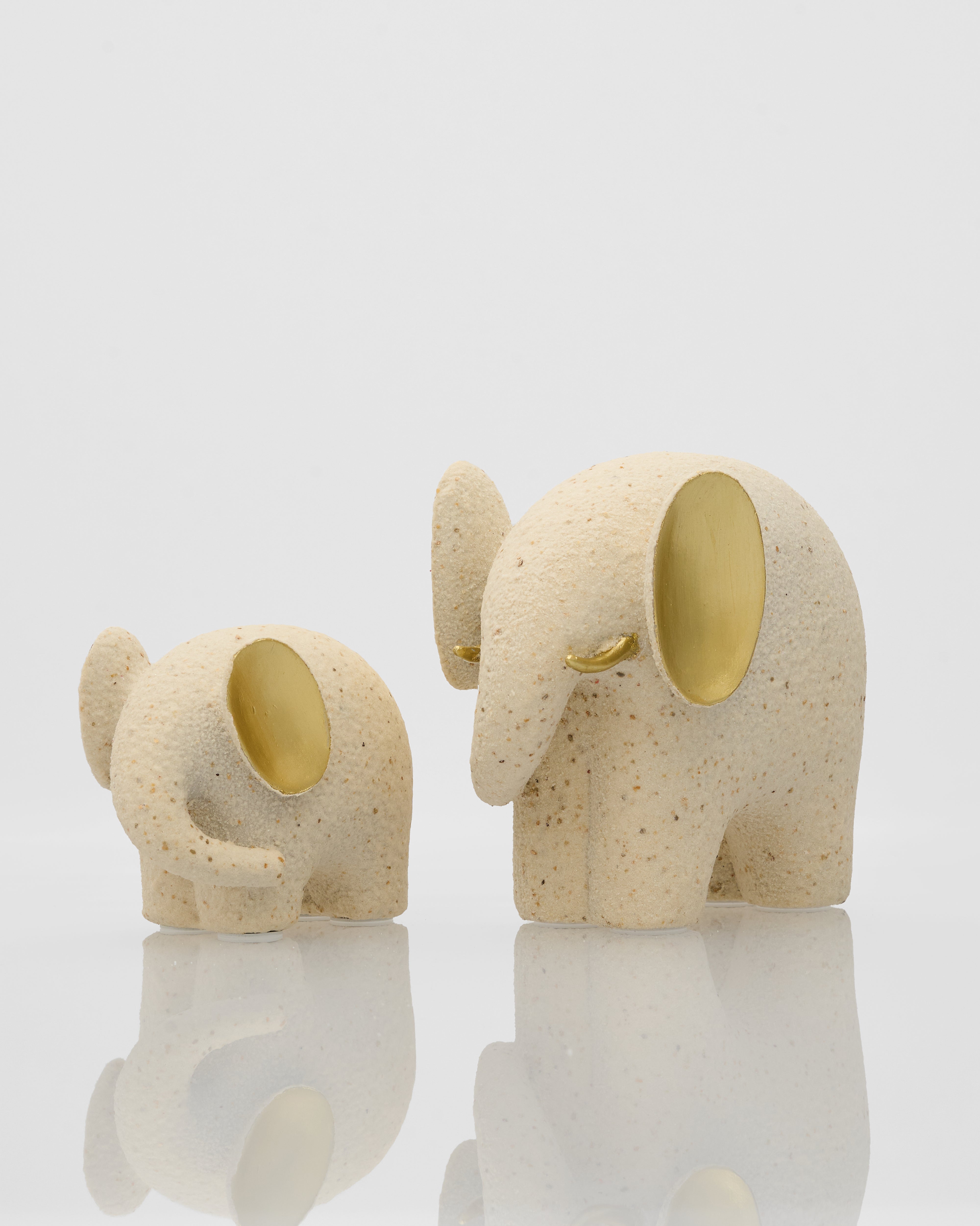 Two ceramic elephant-shaped candle holders with gold interiors on a reflective surface.