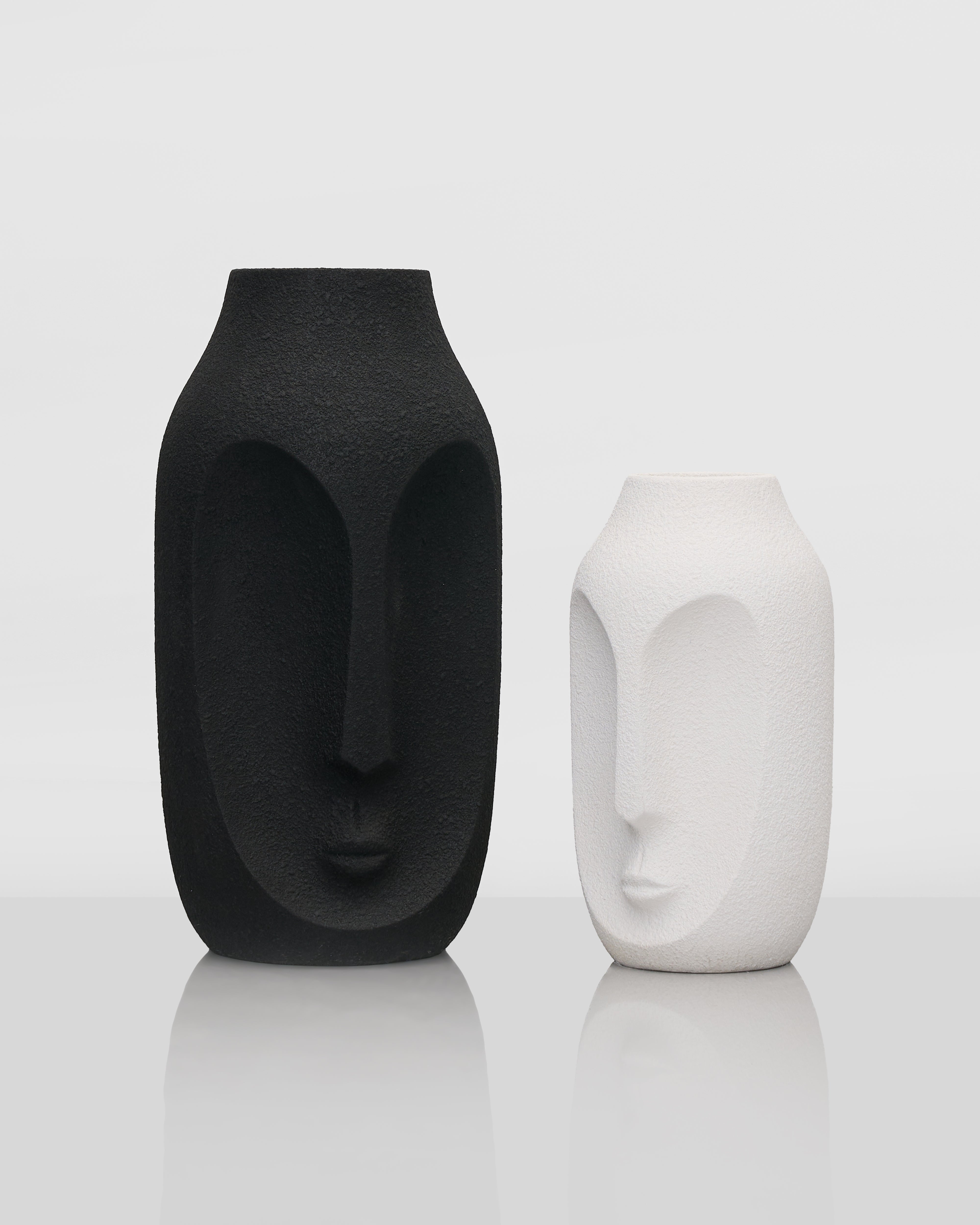 Two face-shaped vases, one black and one white, on a reflective surface with a light gray background.