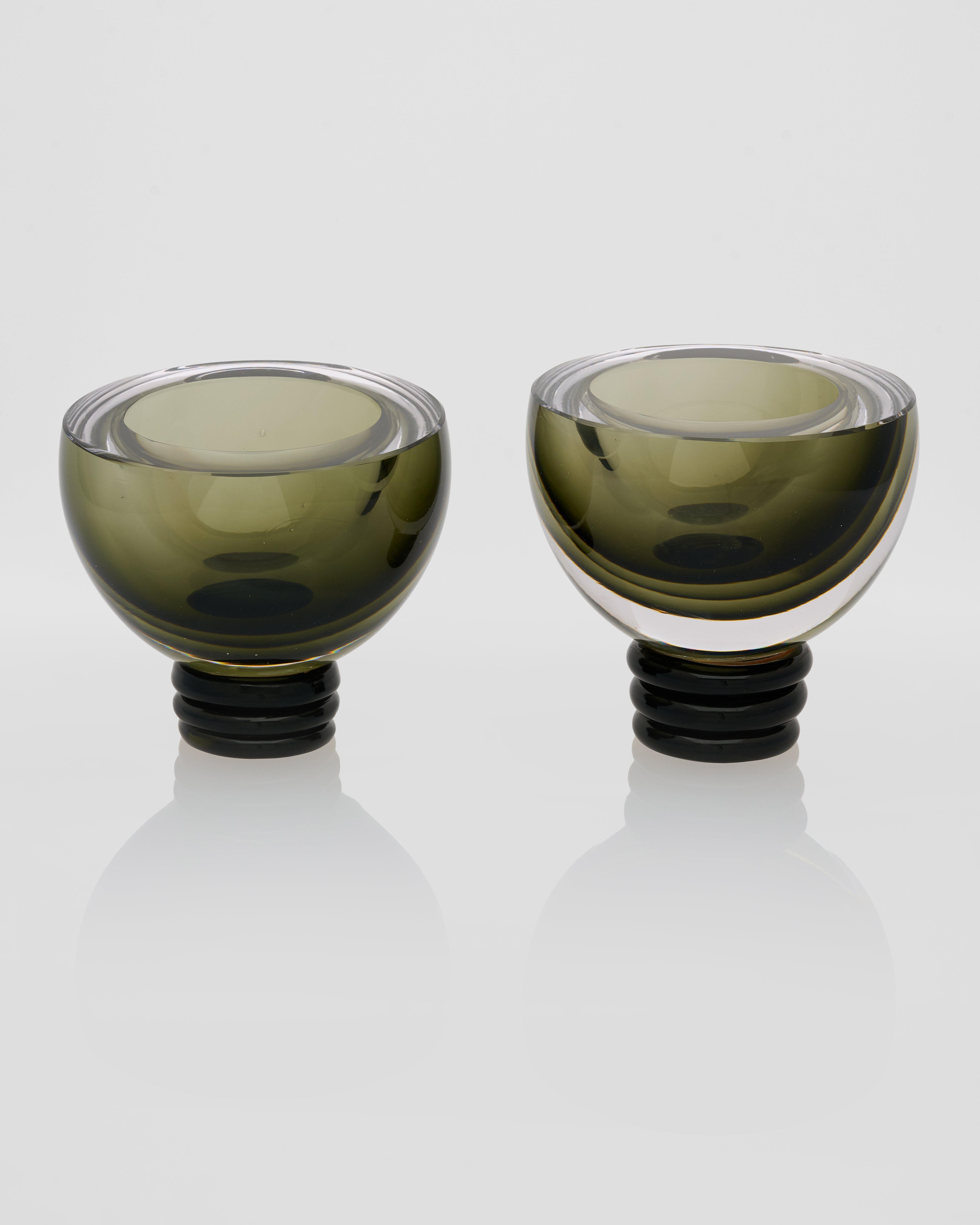 Two green glass candle holders with black bases on a white background