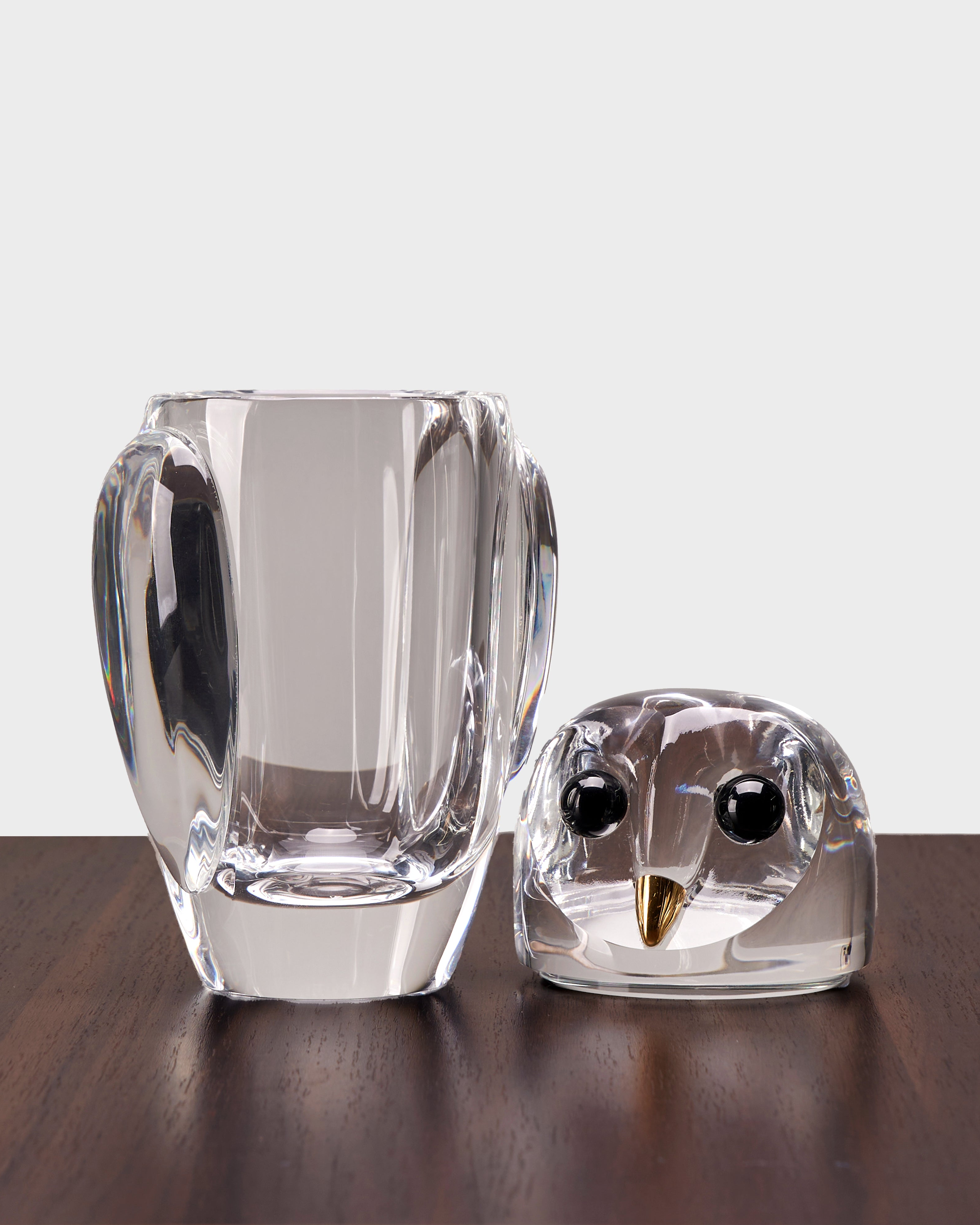 Clear glass owl figurine and vase on a wooden surface with a white background