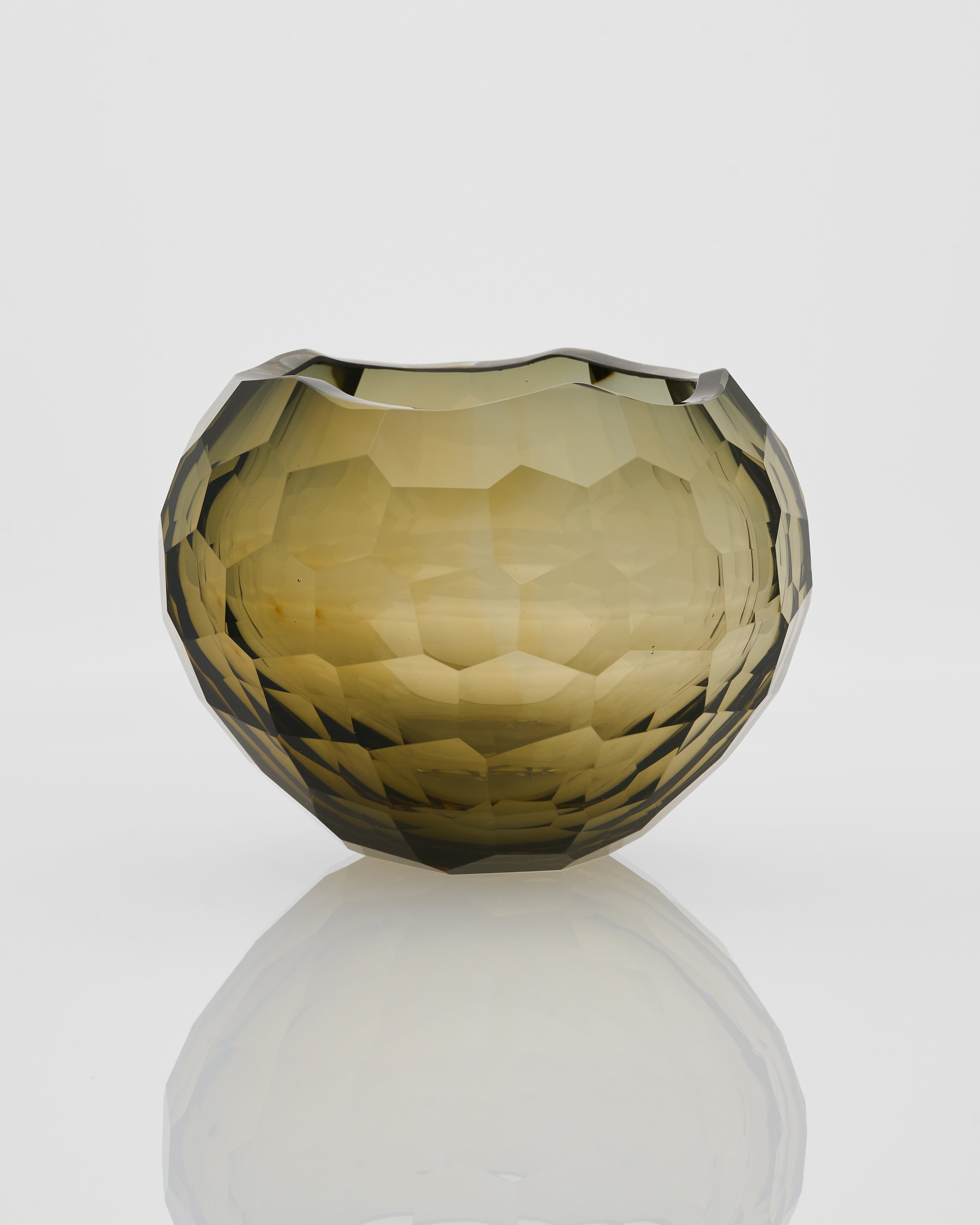 Faceted glass vase on a reflective surface with a light gray background