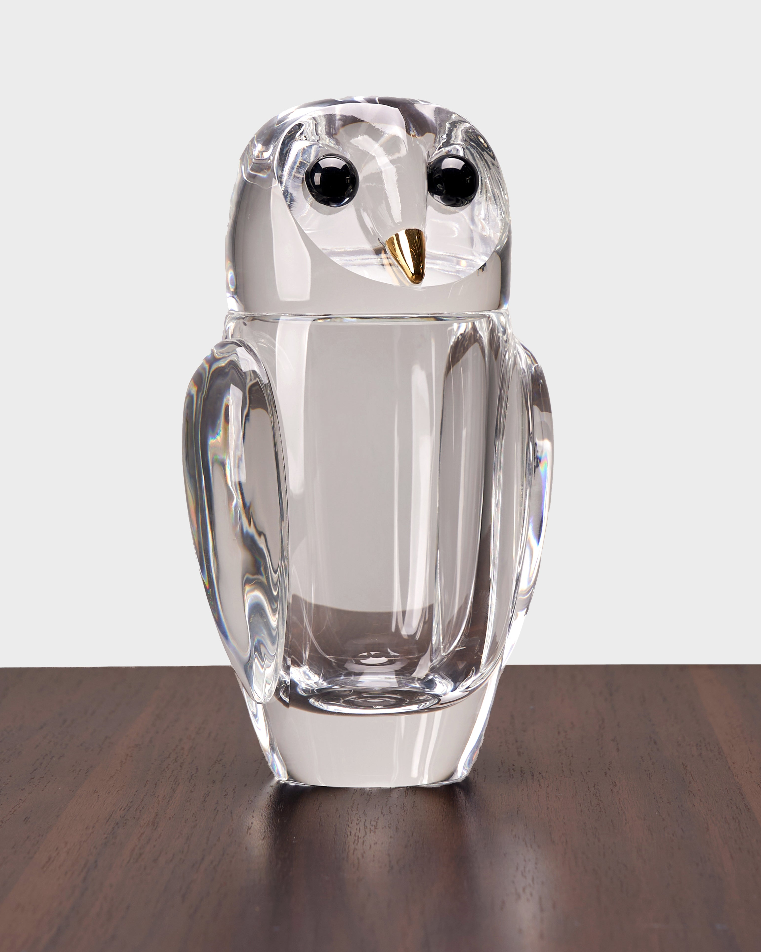 Clear glass owl figurine on a wooden surface with a white background