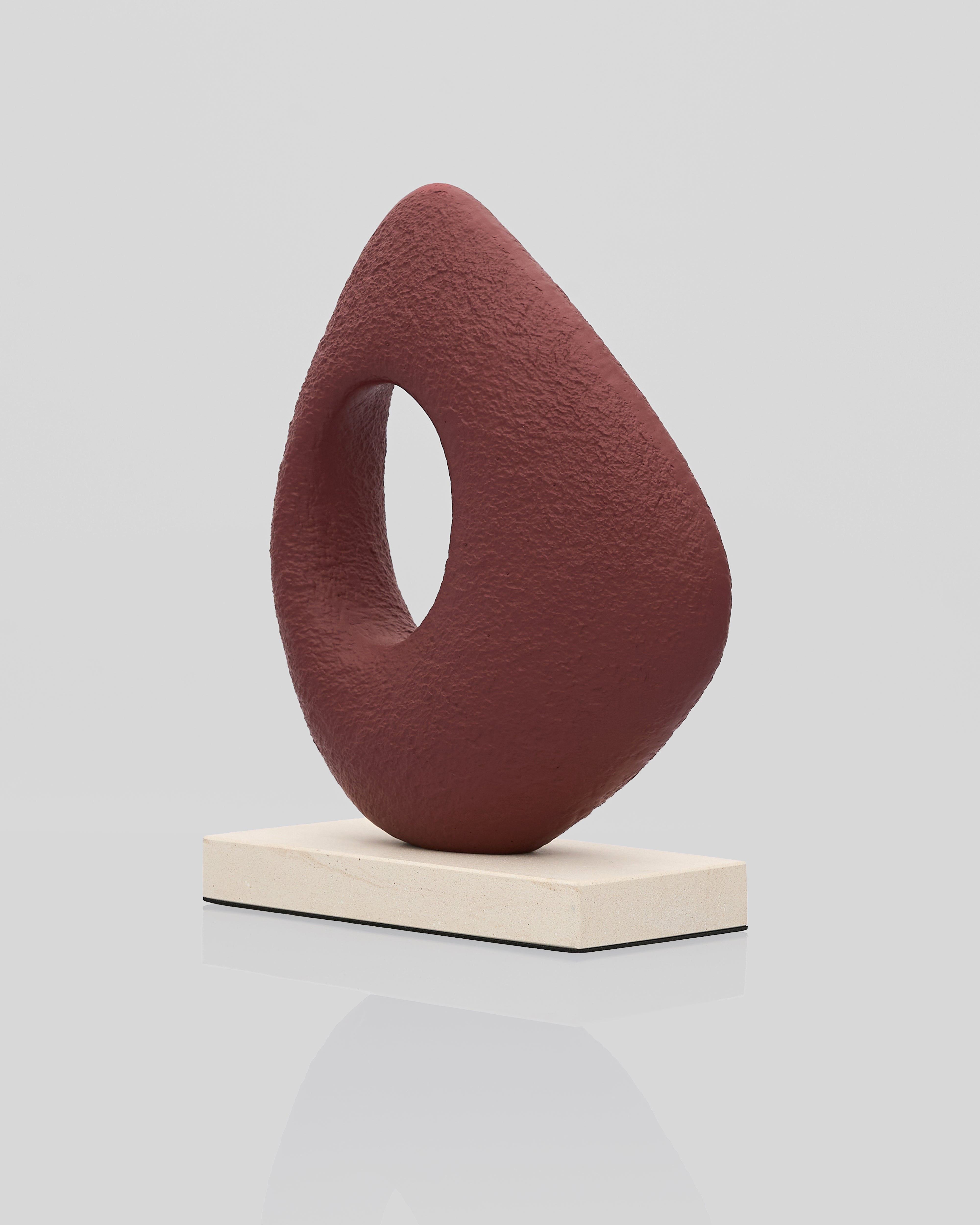 Abstract brown sculpture on a white platform against a light gray background