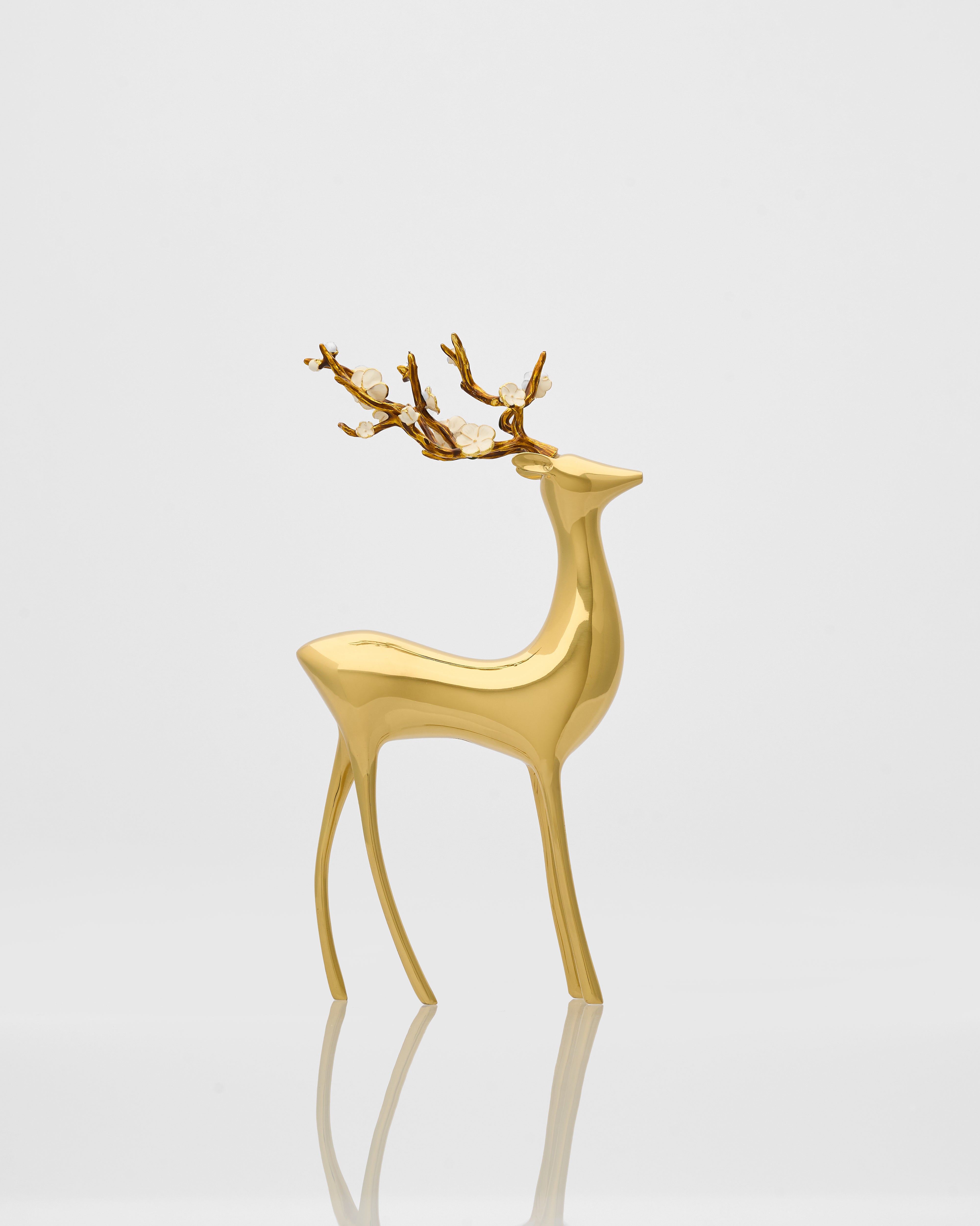 Gold deer figurine on a reflective surface with a light gray background
