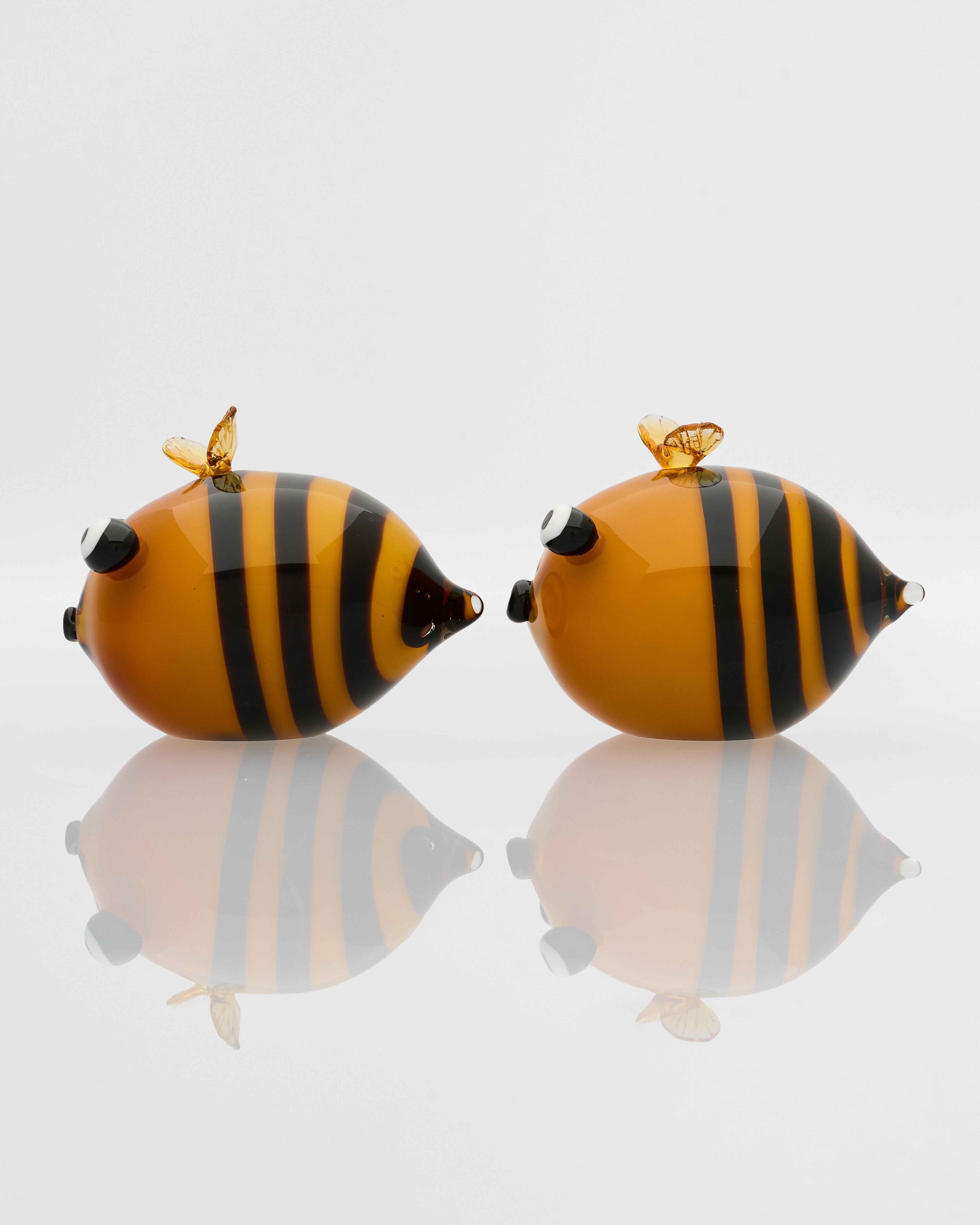 Bee-shaped earrings with black and orange stripes on a reflective surface.