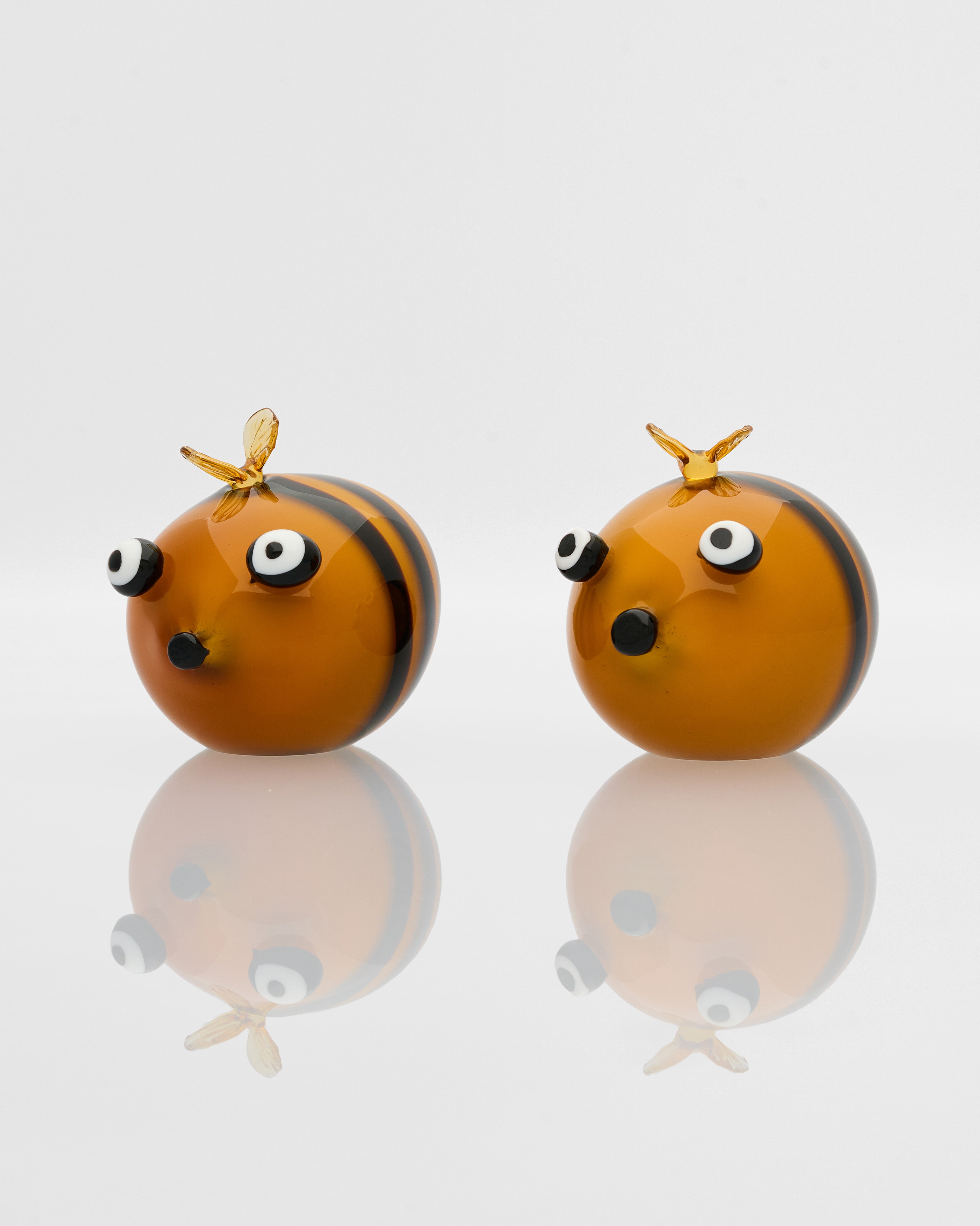 Two small bee-shaped objects with reflective surface on a white background