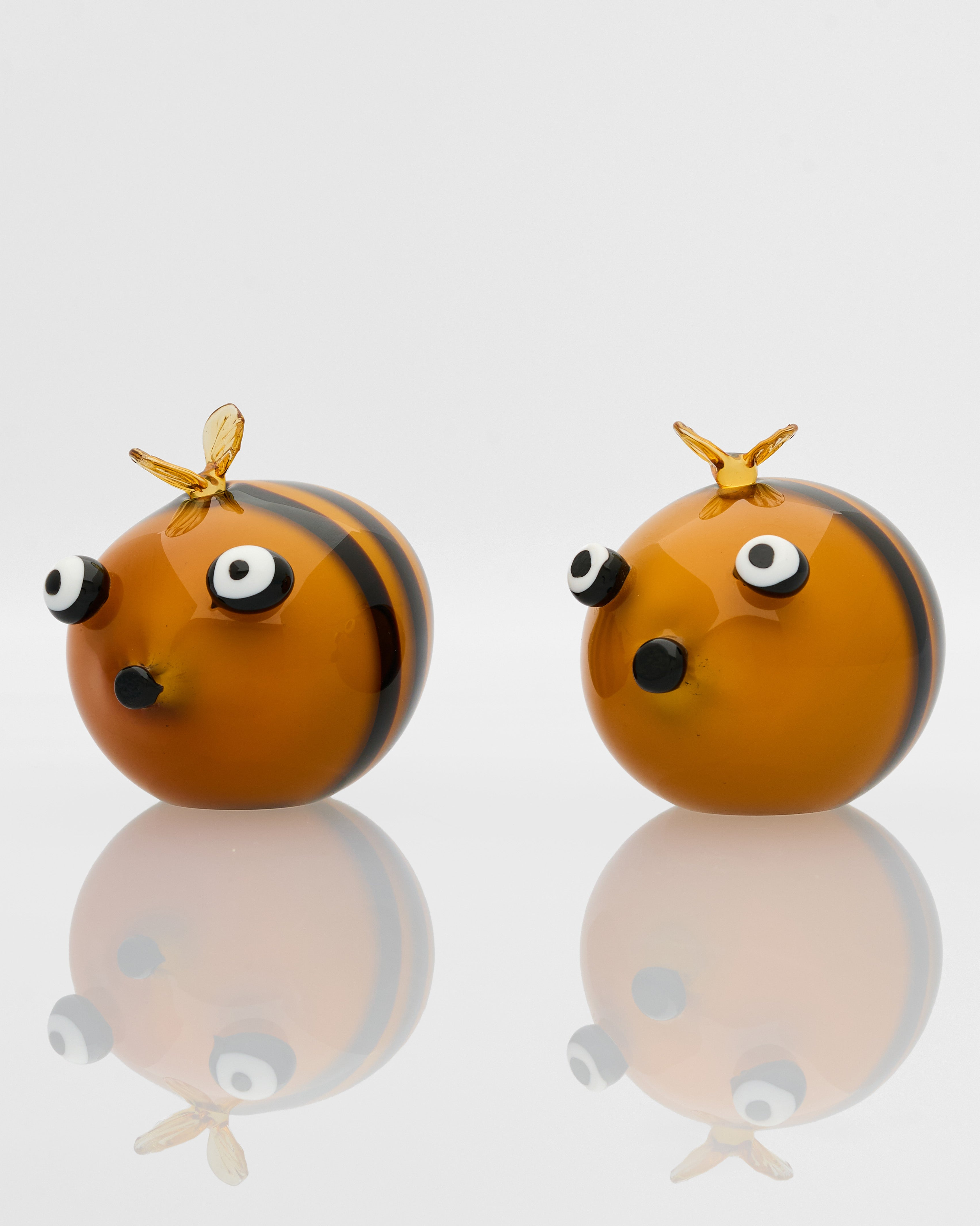 Two bee-shaped figurines with black and yellow stripes on a reflective surface.