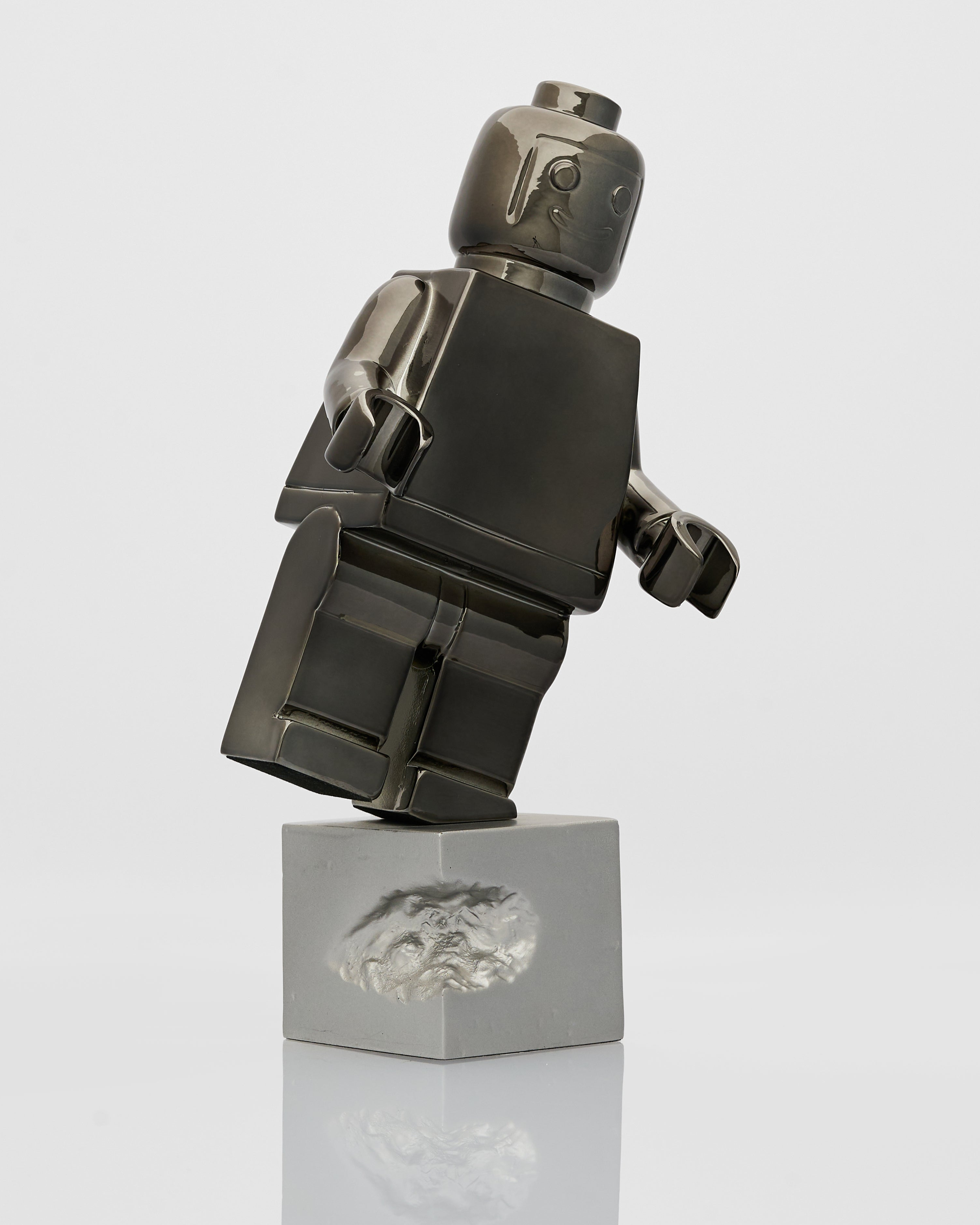 Black and silver Lego figure on a reflective surface with a white background