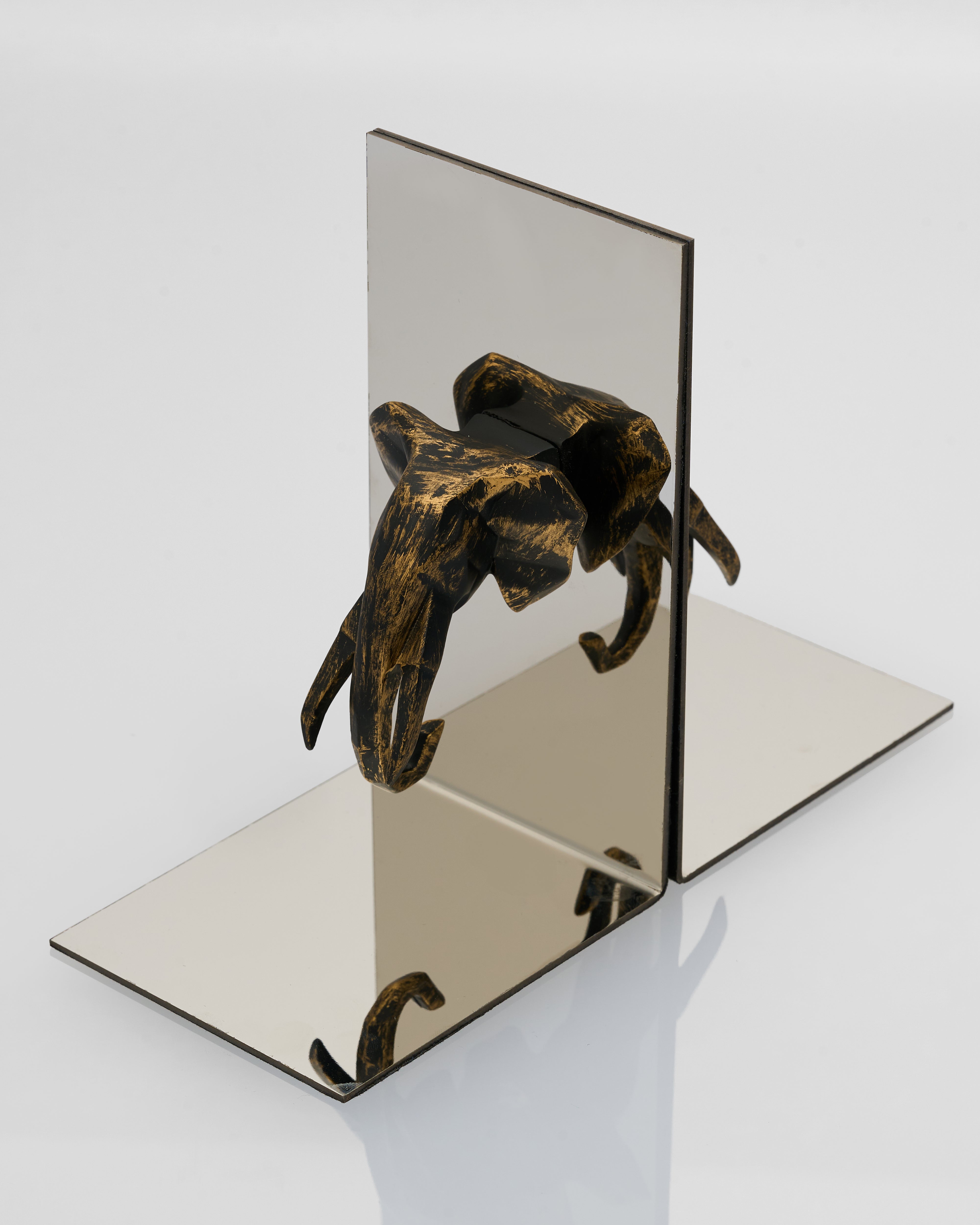 Bronze elephant bookend on a mirrored surface with a white background