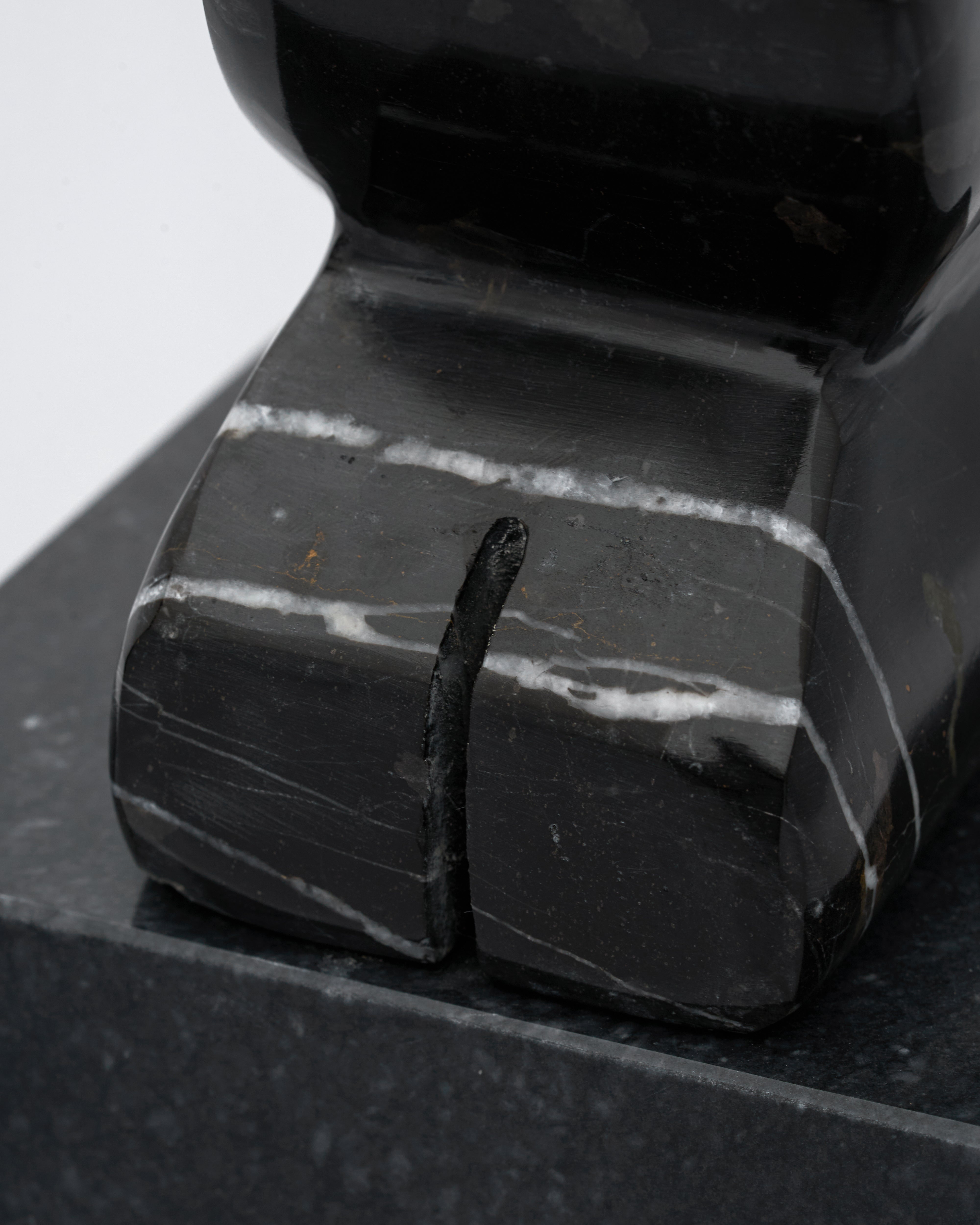 Close-up of a black stone with a nail embedded in it on a dark surface.