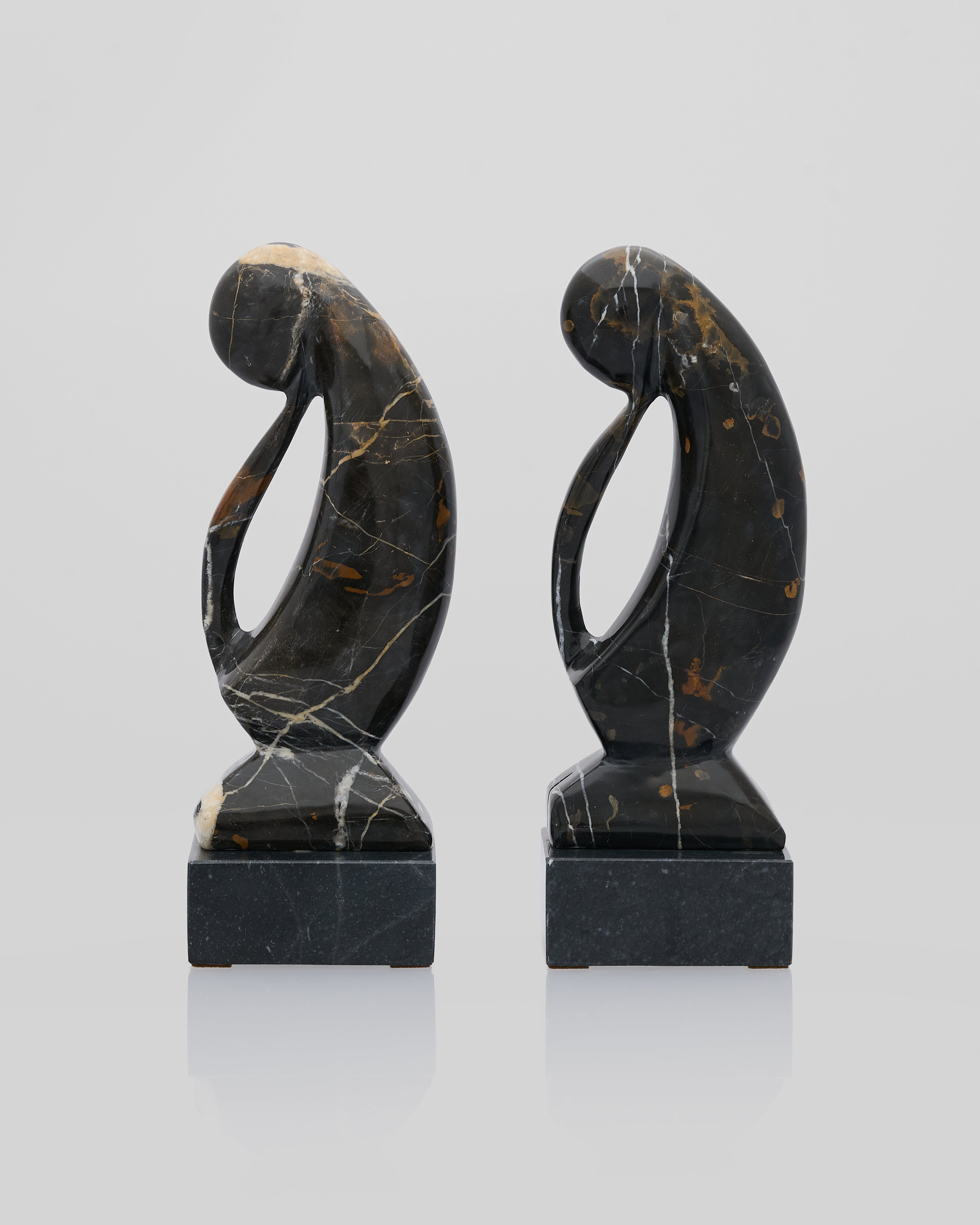 Two abstract marble sculptures on a reflective surface with a light gray background