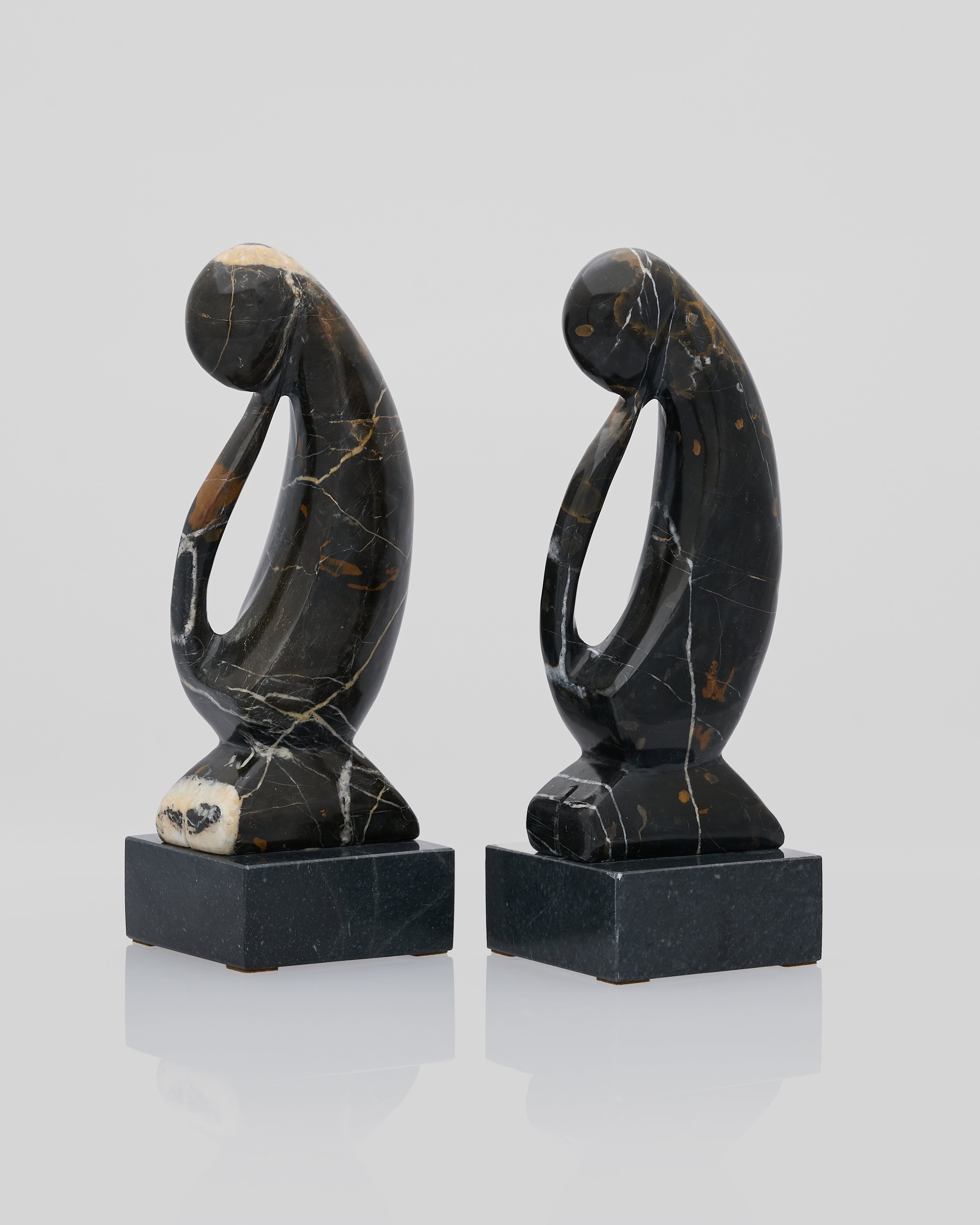 Two abstract stone sculptures on a reflective surface with a light gray background