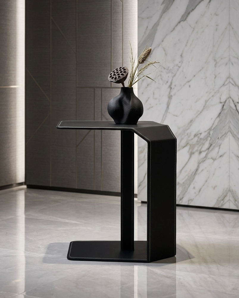 Modern black side table with a vase and dried plants against a marble wall.