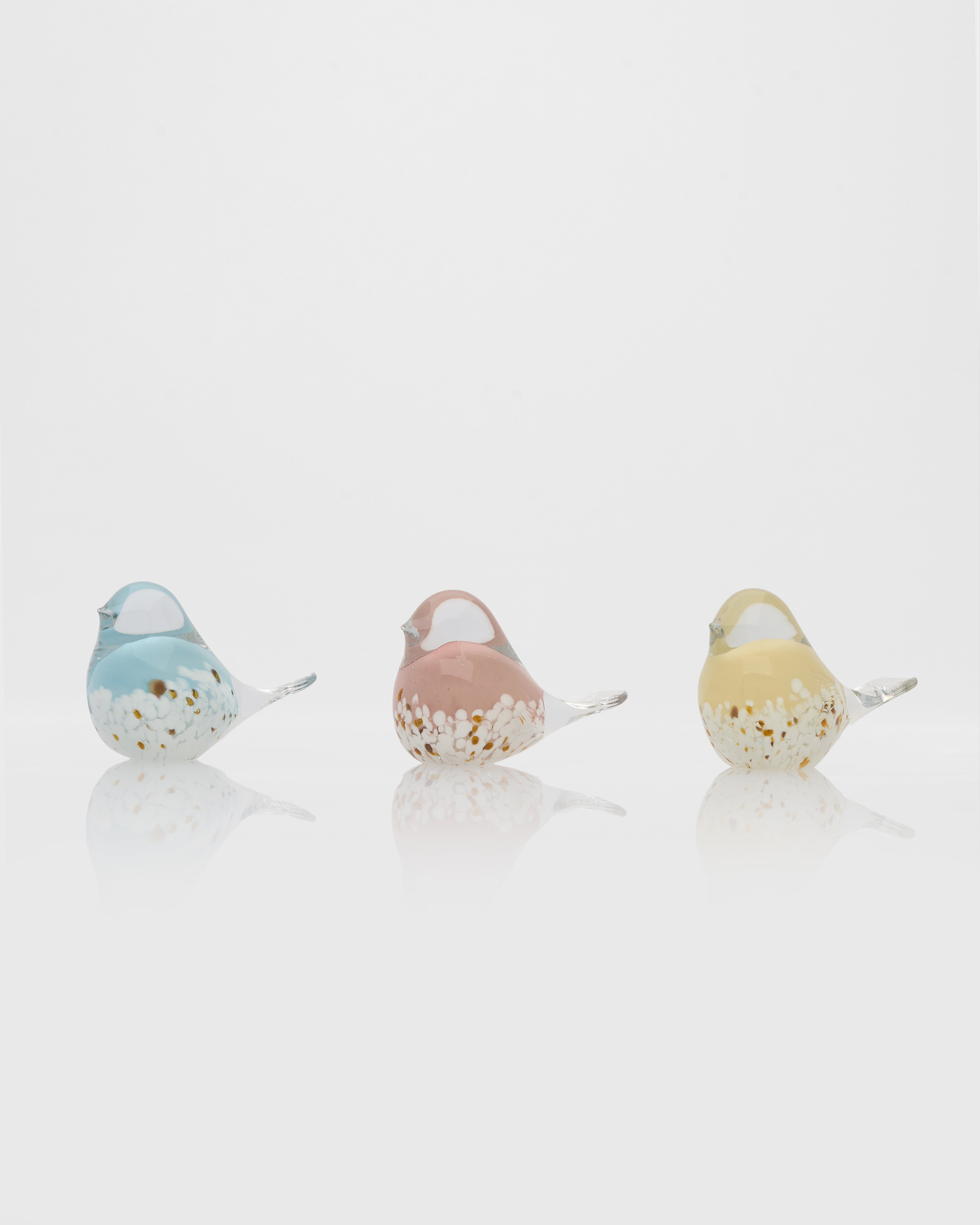 Three glass bird figurines in blue, pink, and yellow on a white background