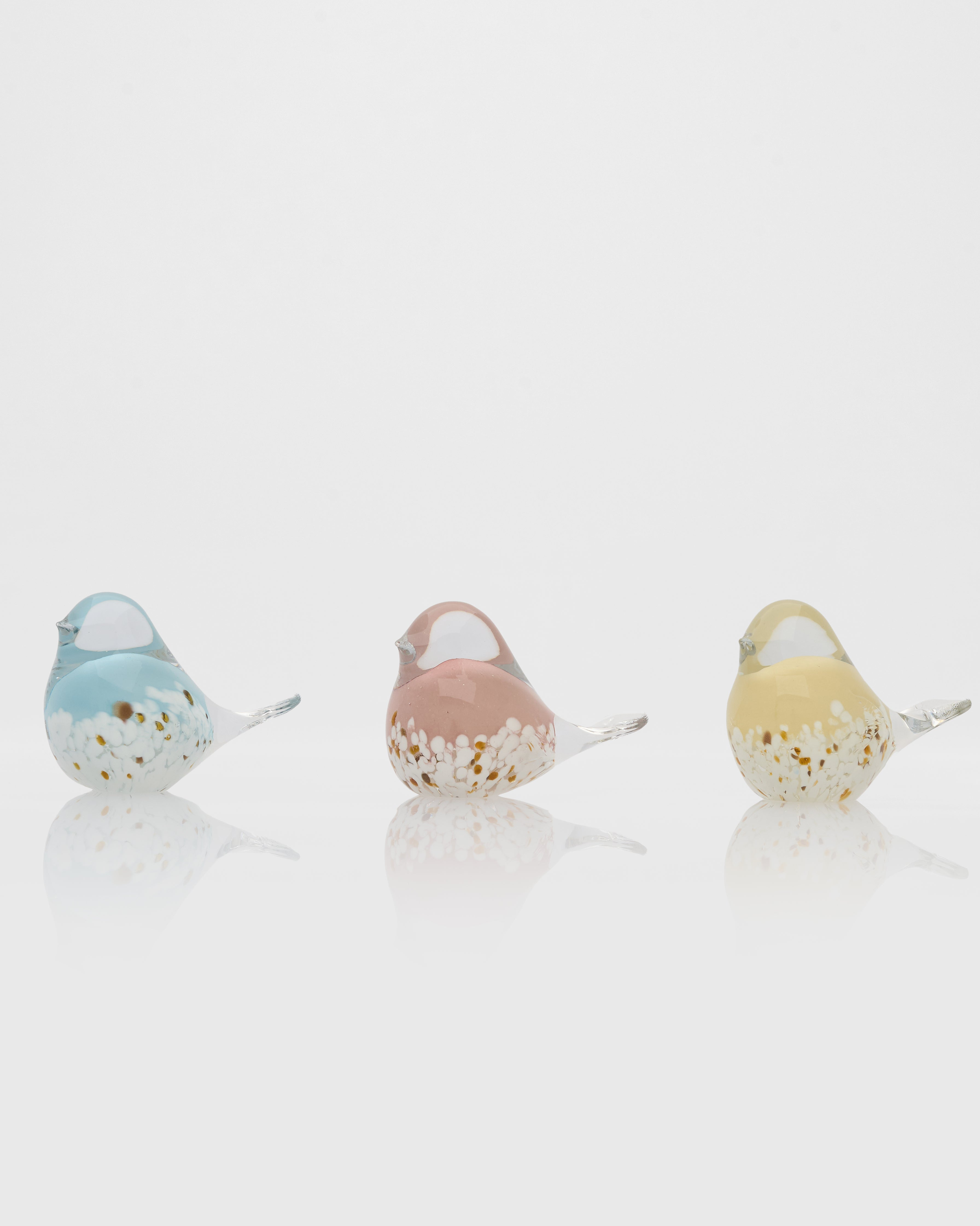 Three small bird figurines in pastel colors on a white background