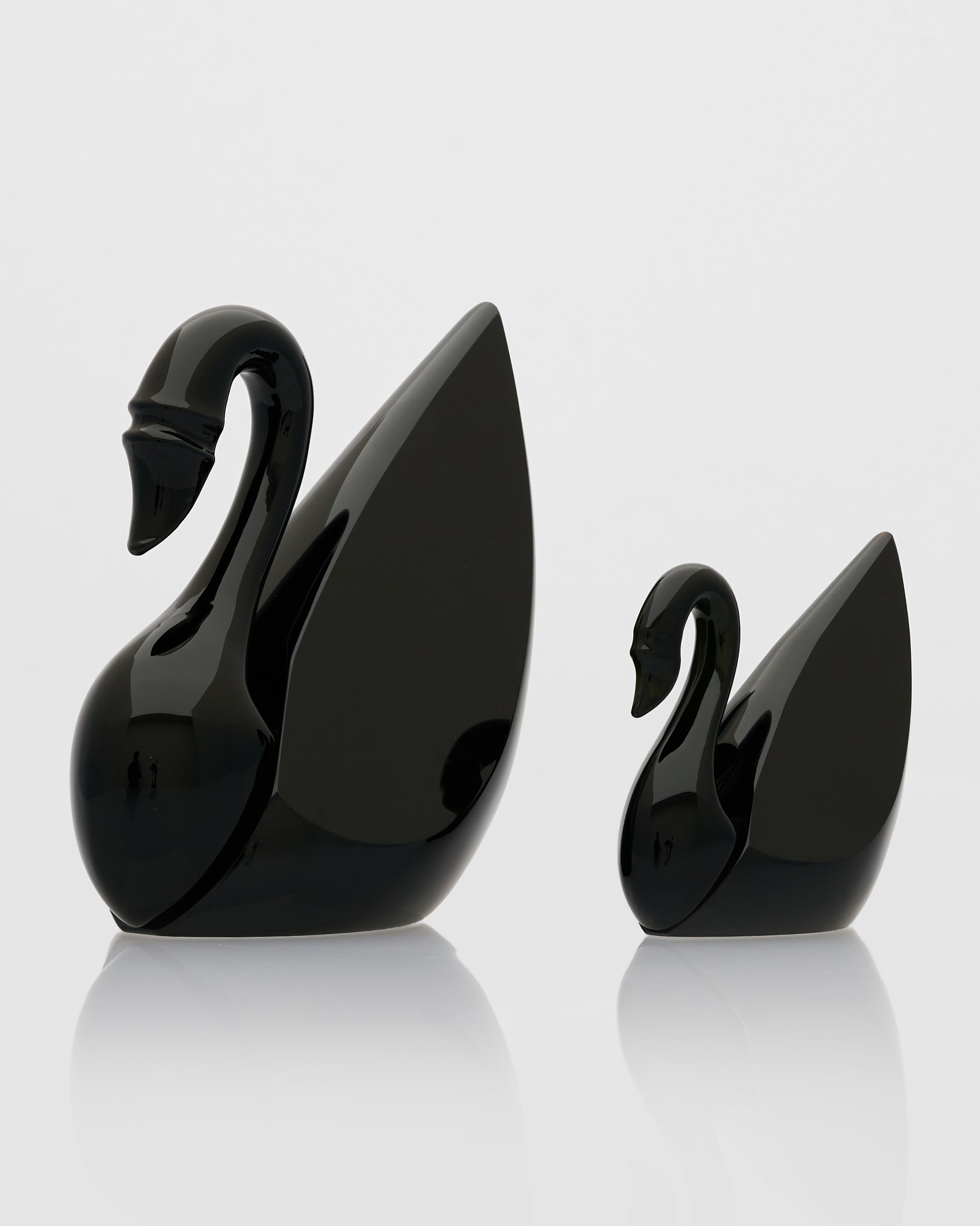 Two black swan-shaped objects on a reflective surface with a light gray background