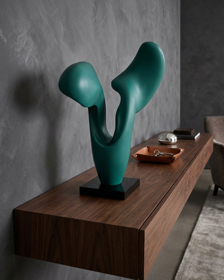 Teal abstract sculpture on a wooden shelf against a gray wall.