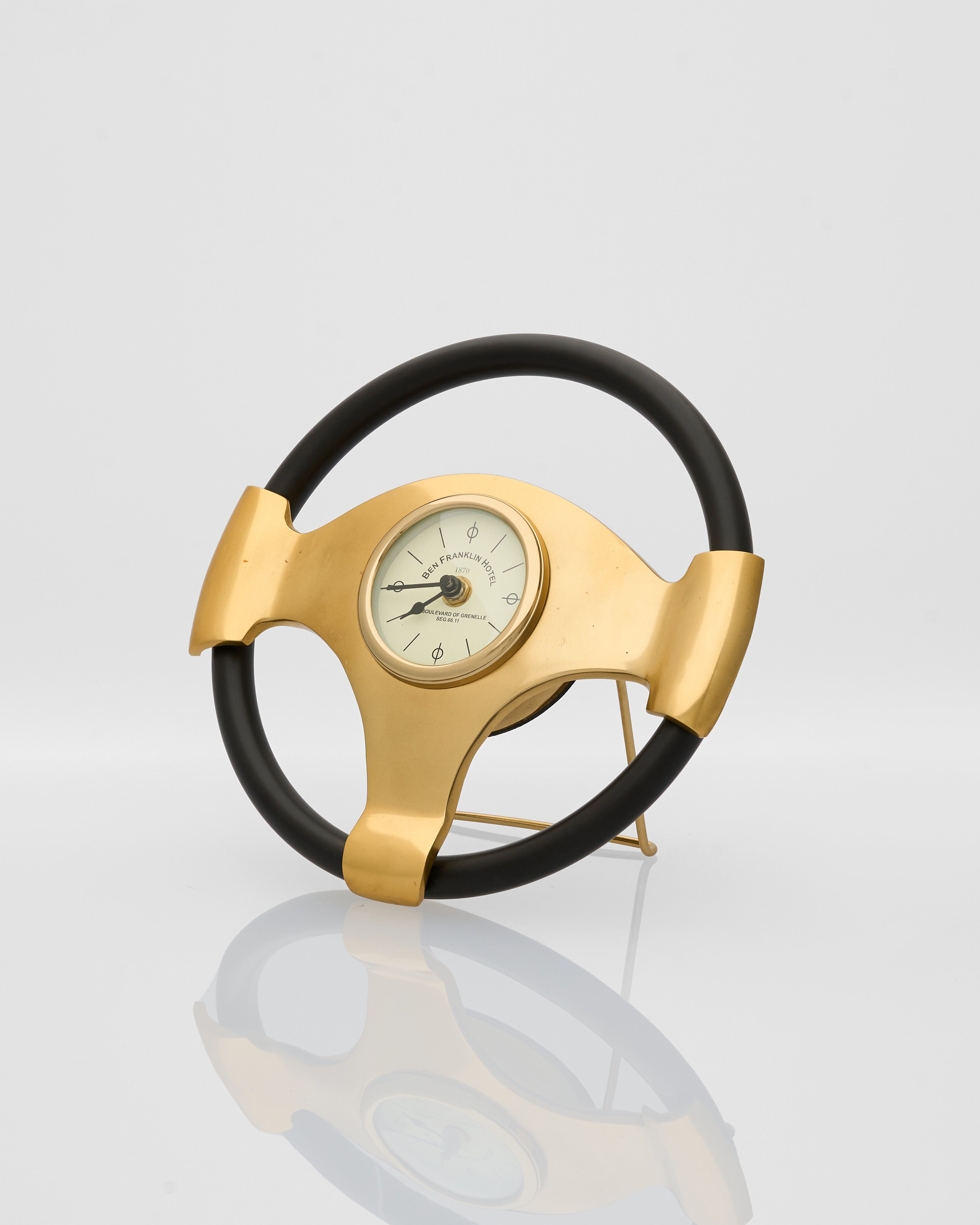 Steering wheel-shaped clock with gold rim and black rim on a reflective surface