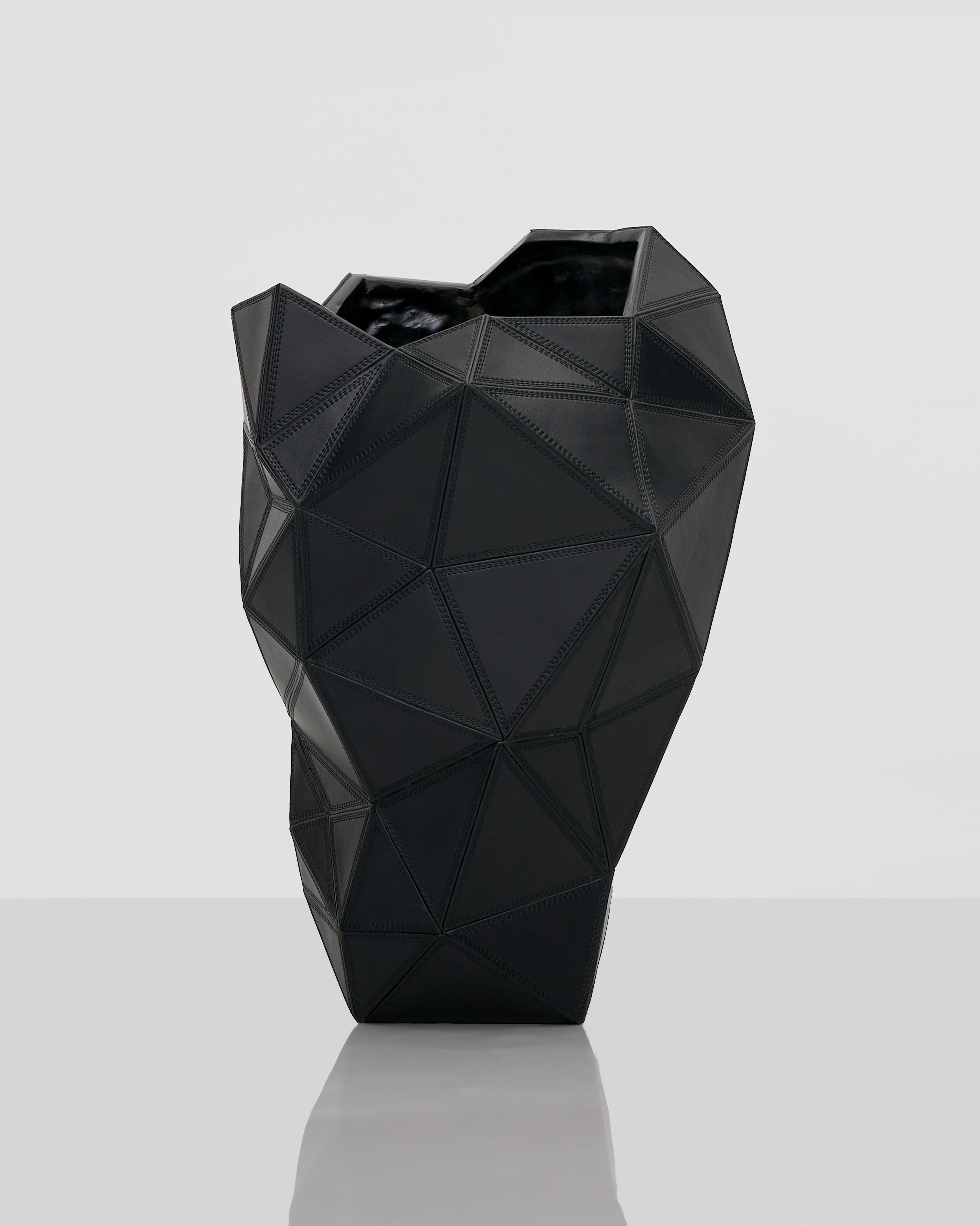 Black geometric vase on a reflective surface with a light gray background