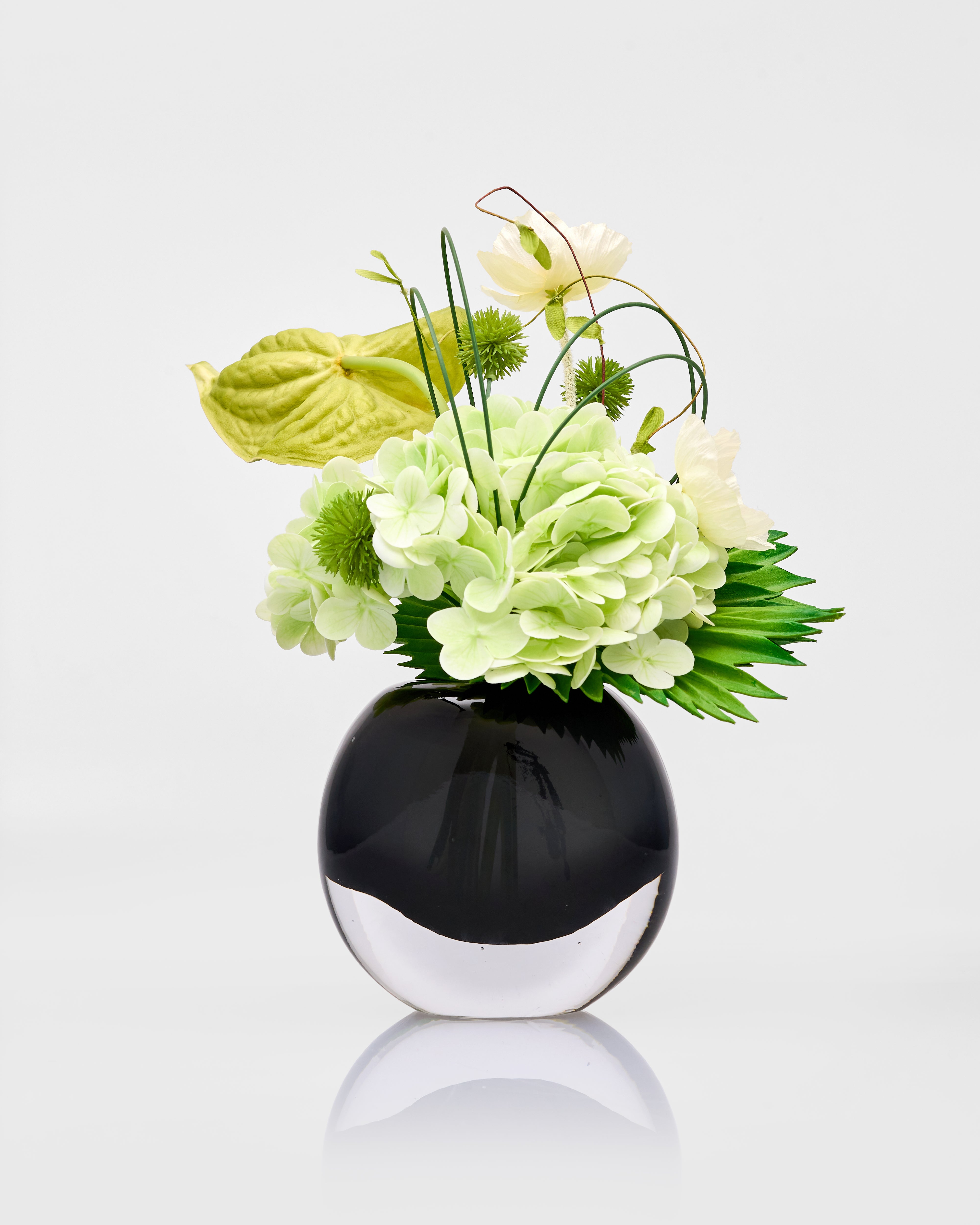 Black vase with green and white flowers on a light gray background