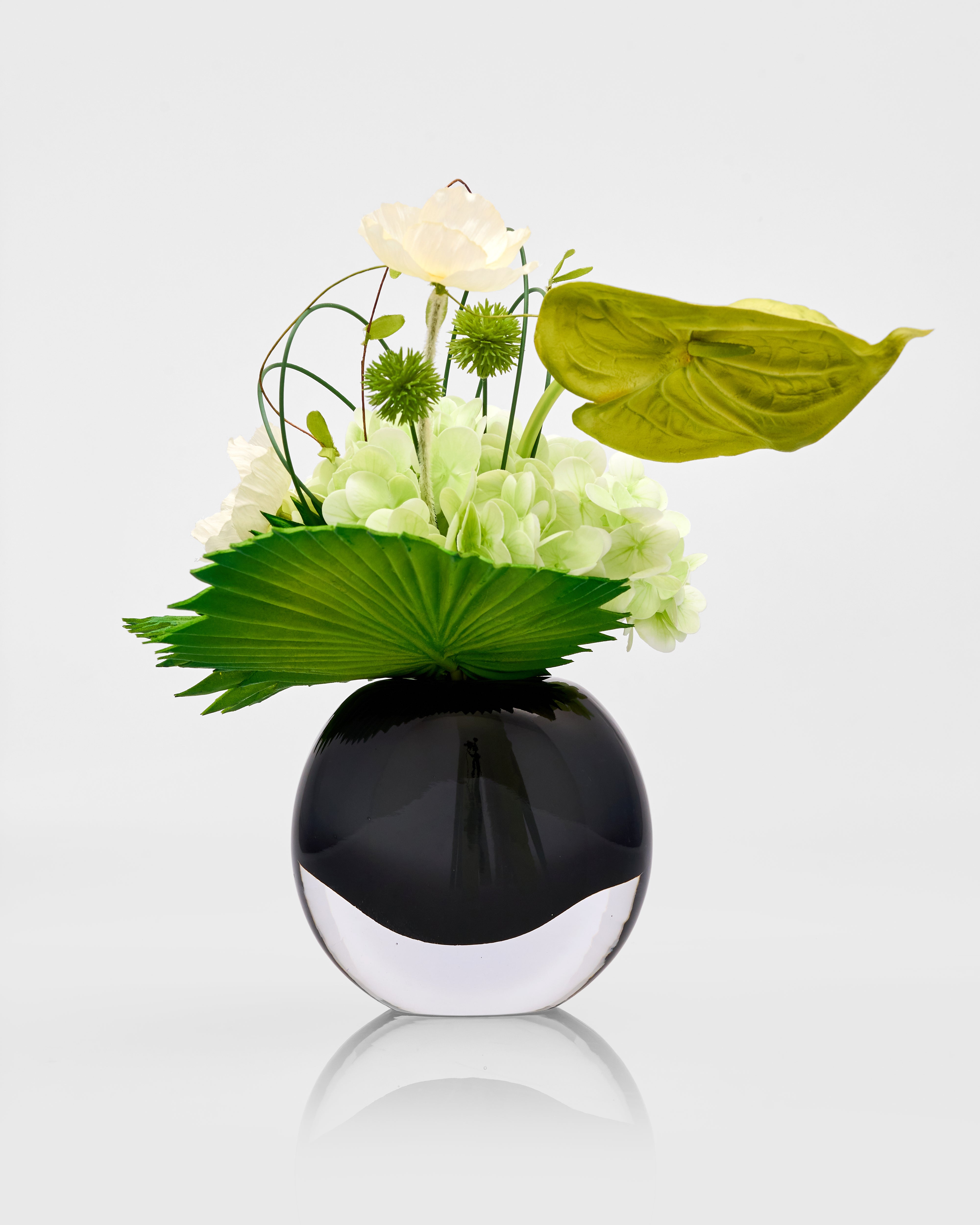 Black vase with green and white flowers on a light gray background