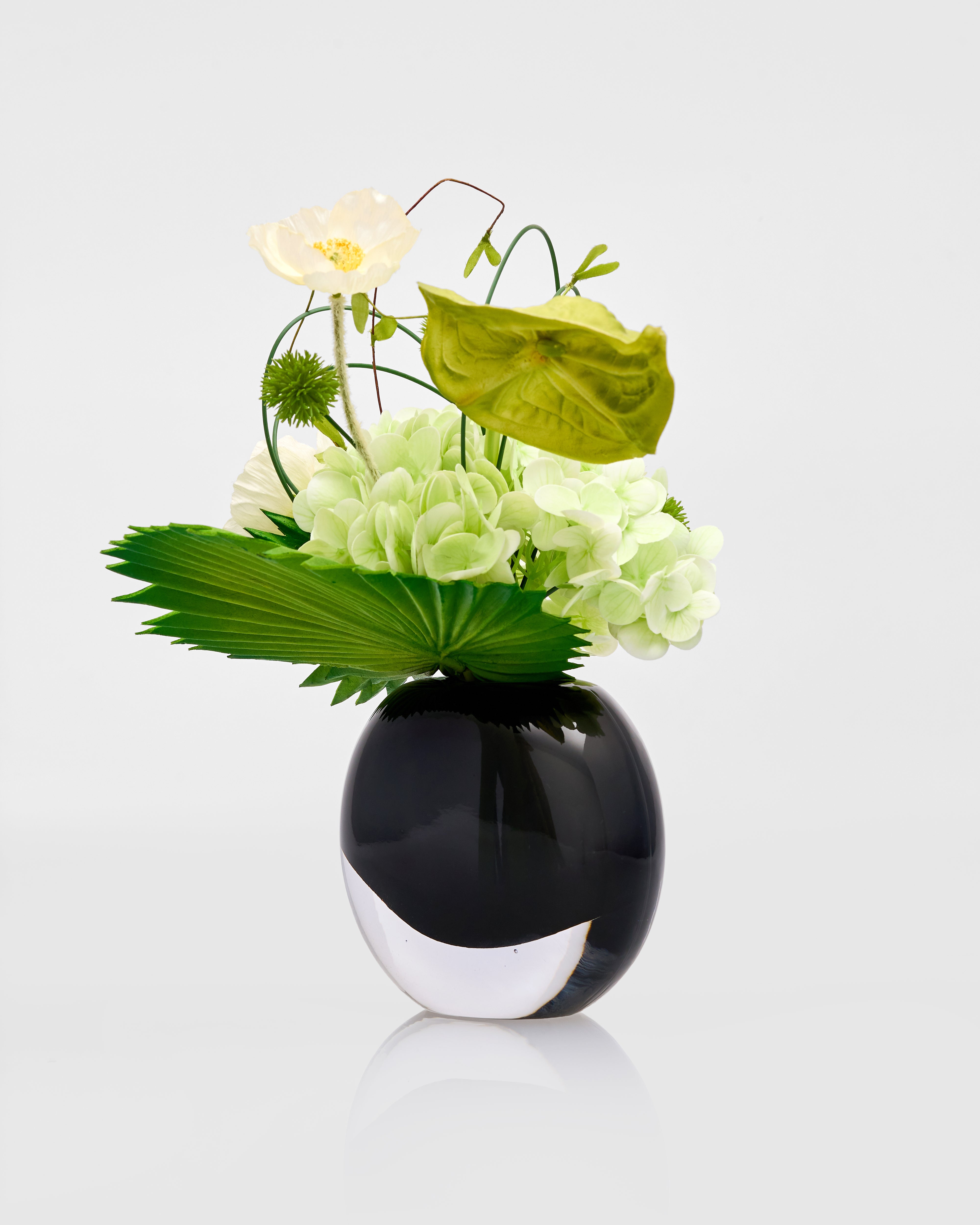 Black vase with green and white flowers on a light gray background