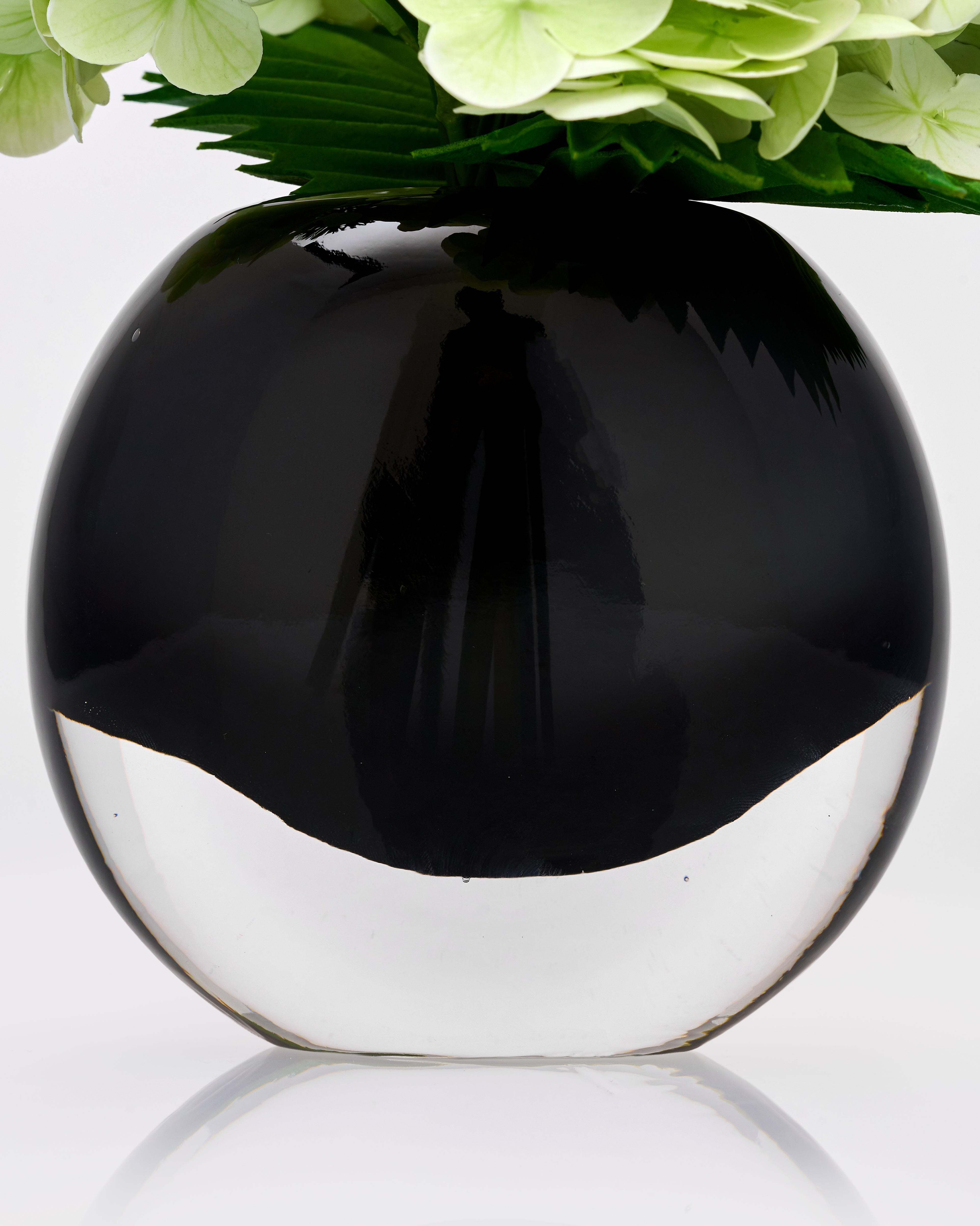 Black spherical vase with a reflective surface, containing green flowers on a white background