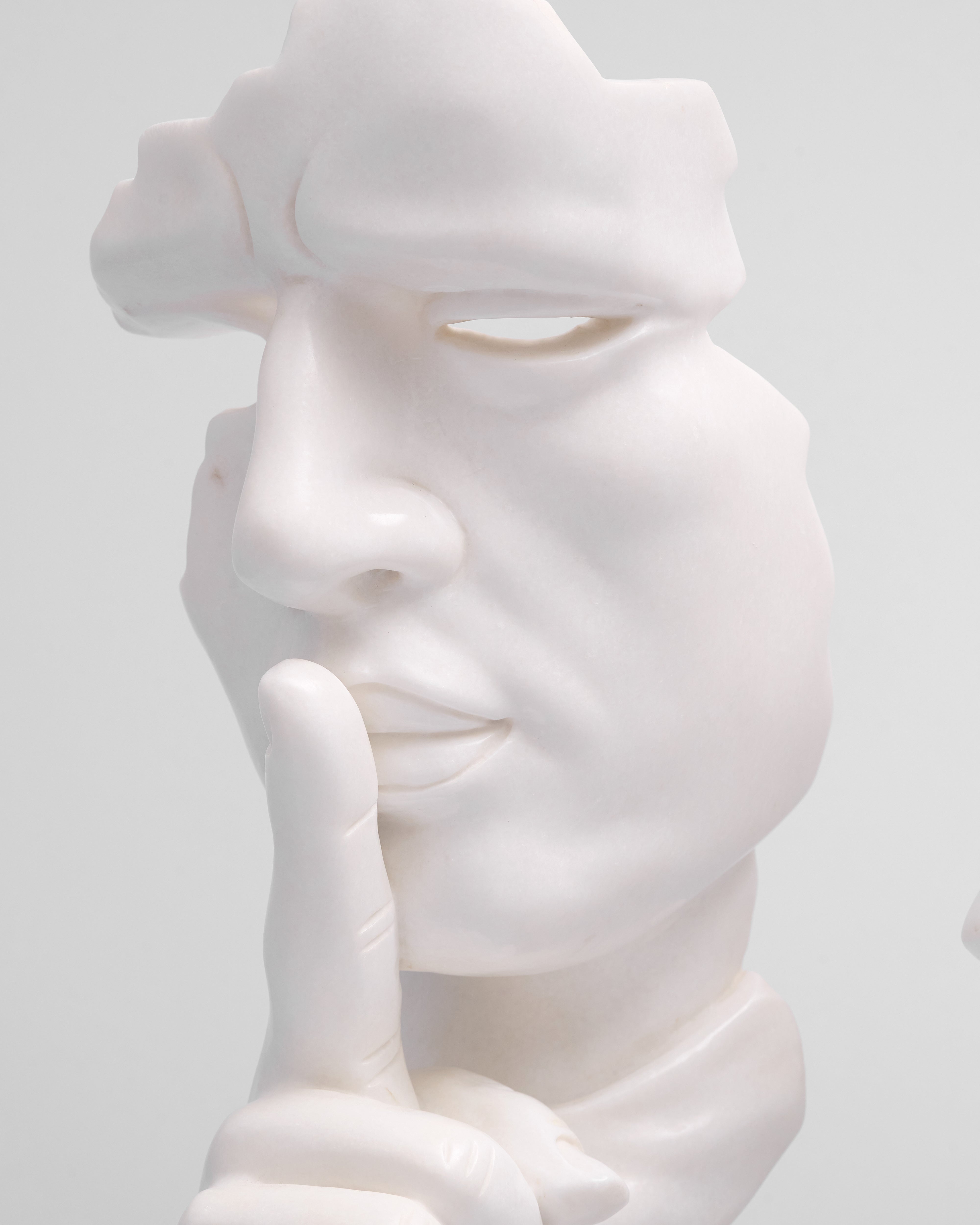 White marble sculpture of a face with a hand on its cheek against a light gray background