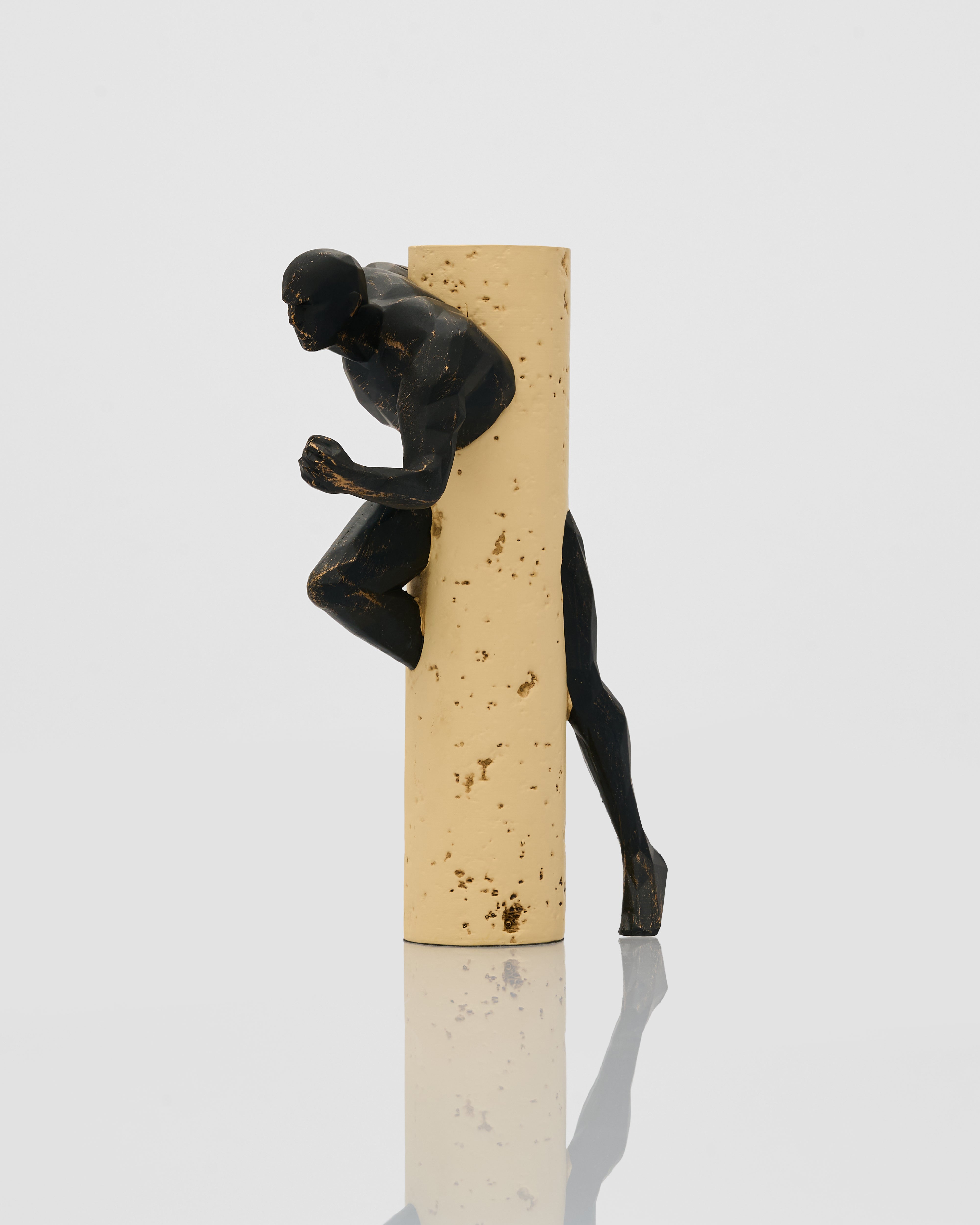 Black figurine climbing a beige cylindrical object on a white background