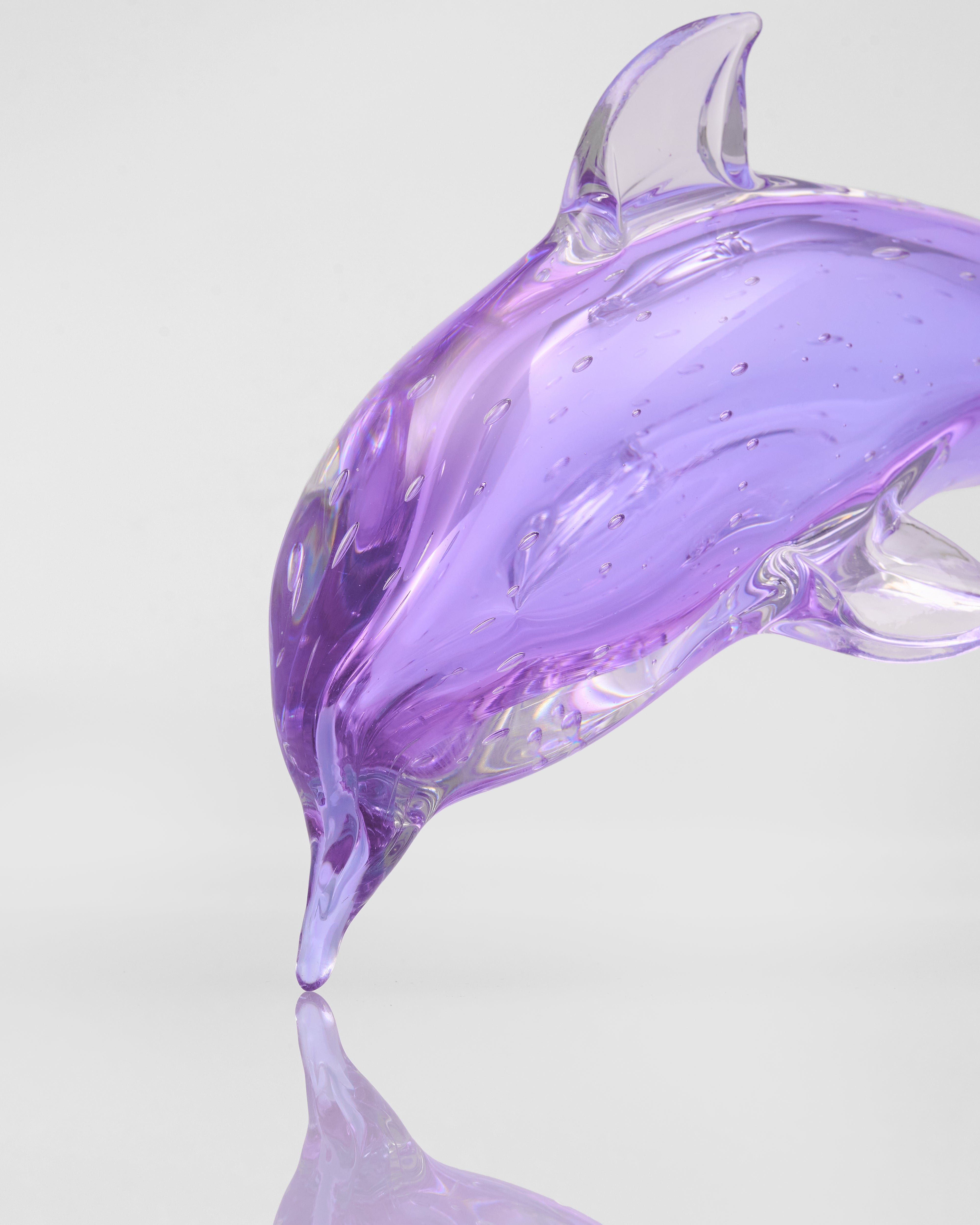 Purple glass dolphin sculpture on a reflective surface with a light gray background