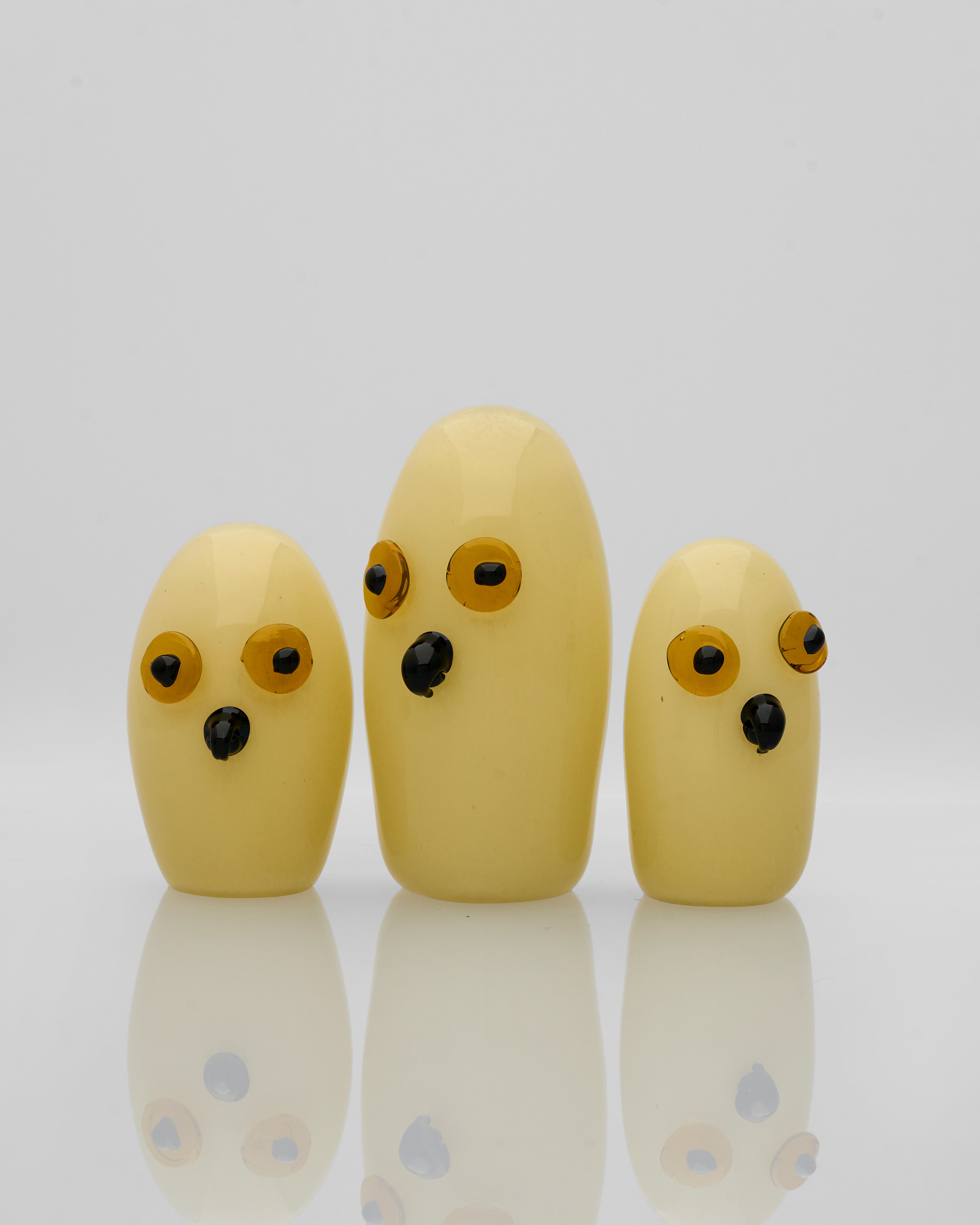 Three bananas with painted faces on a reflective surface