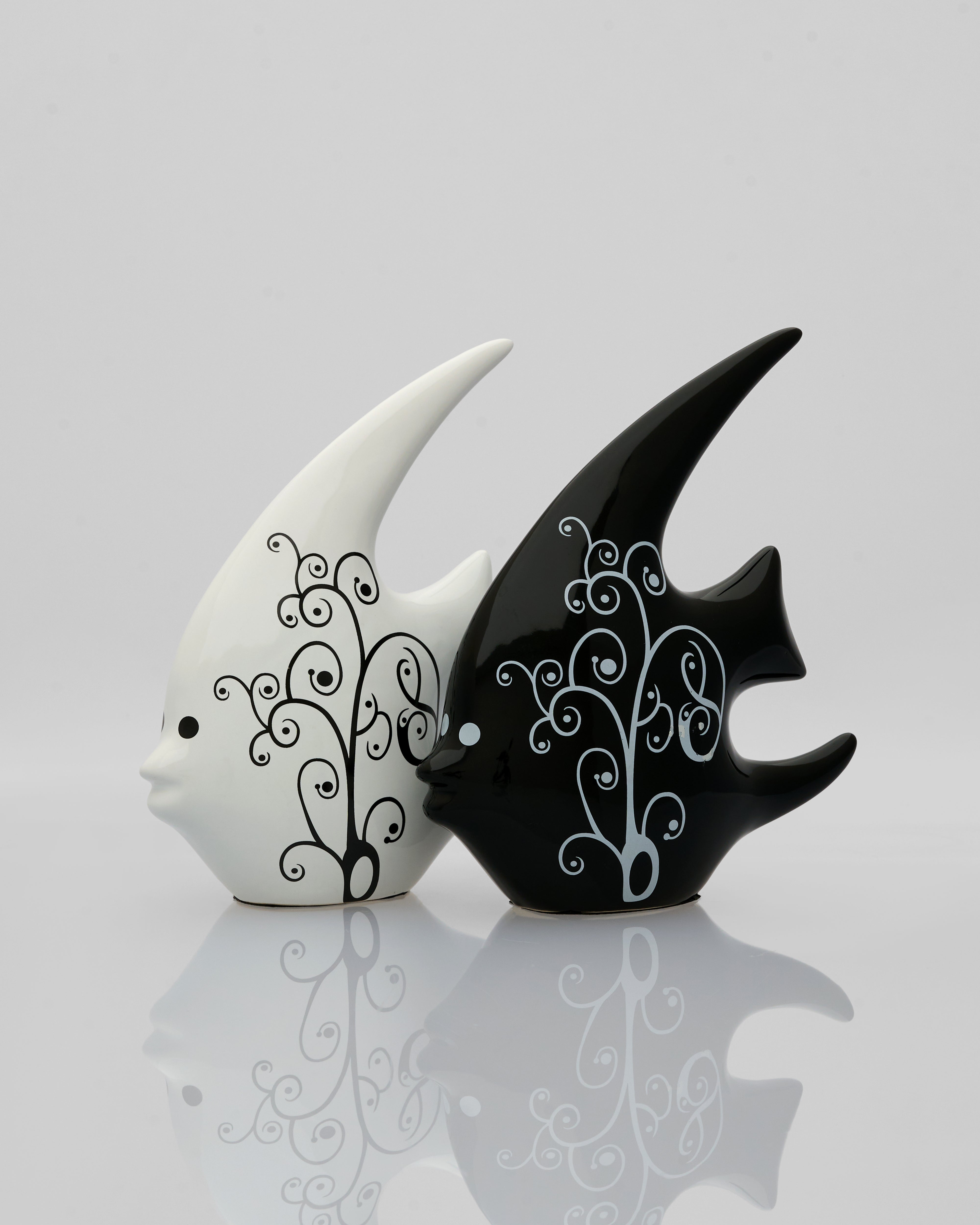 Black and white ceramic fish figurines with decorative patterns on a reflective surface.