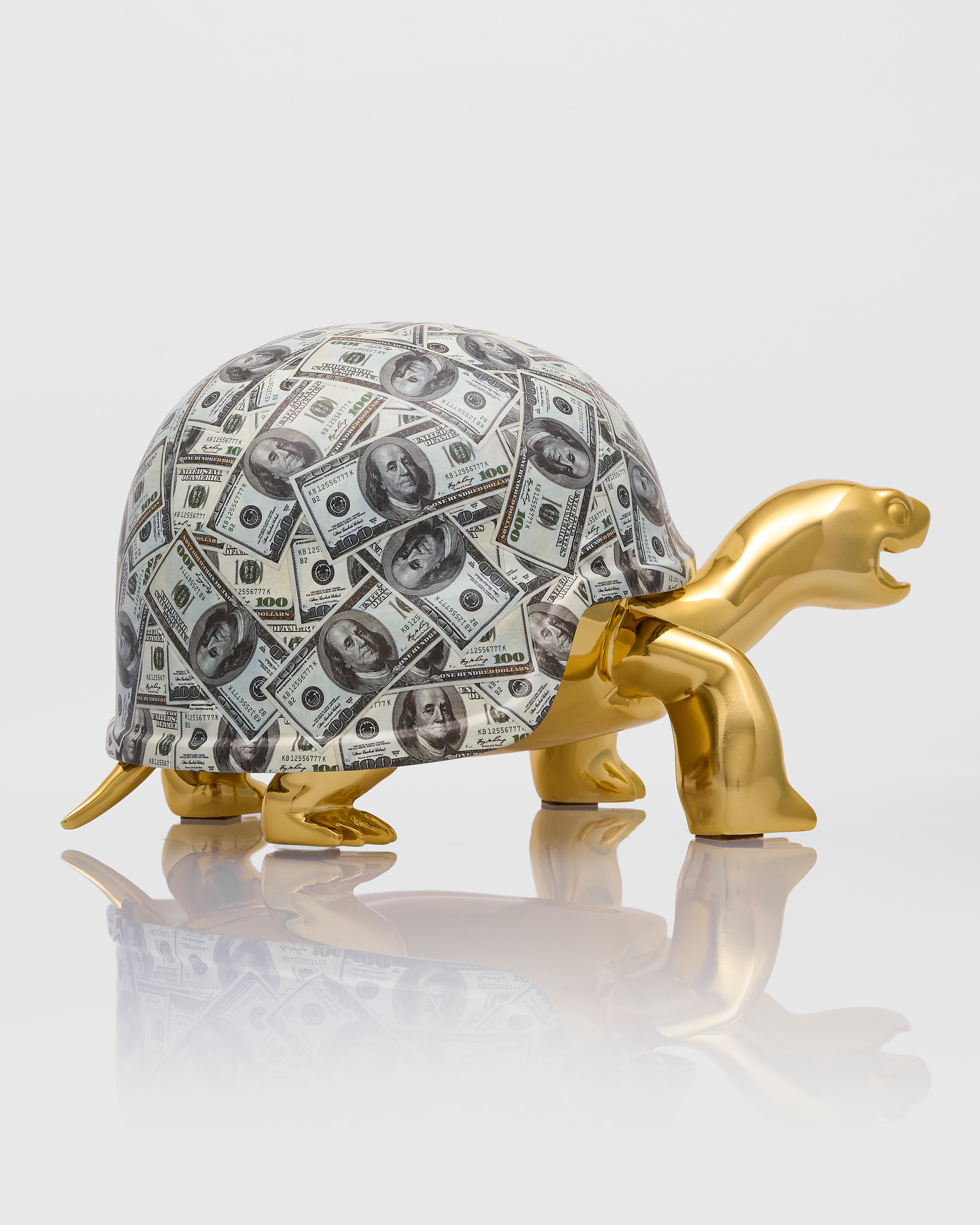 Gold turtle figurine with a shell made of dollar bills on a white background