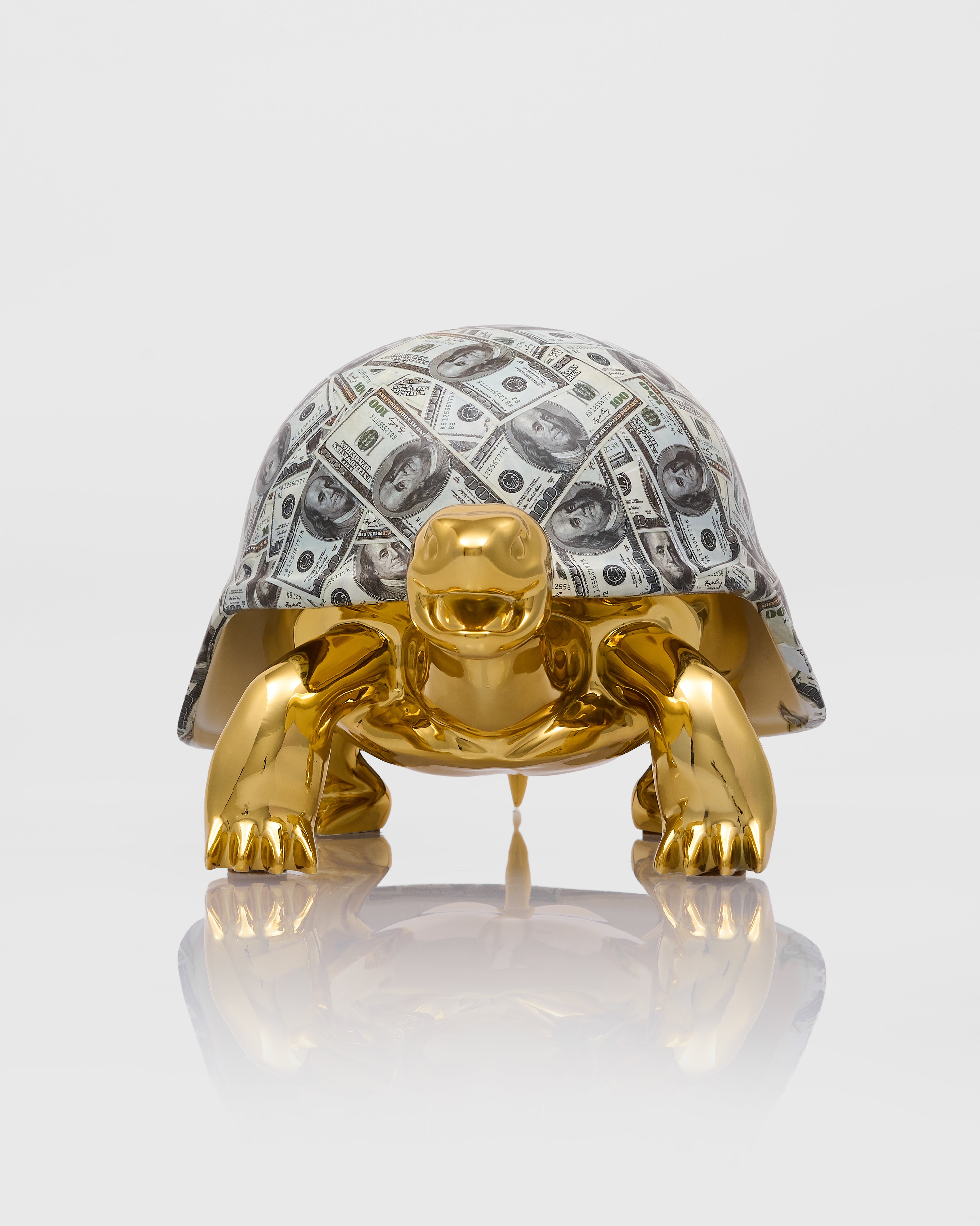 Gold turtle figurine with a shell made of dollar bills on a white background