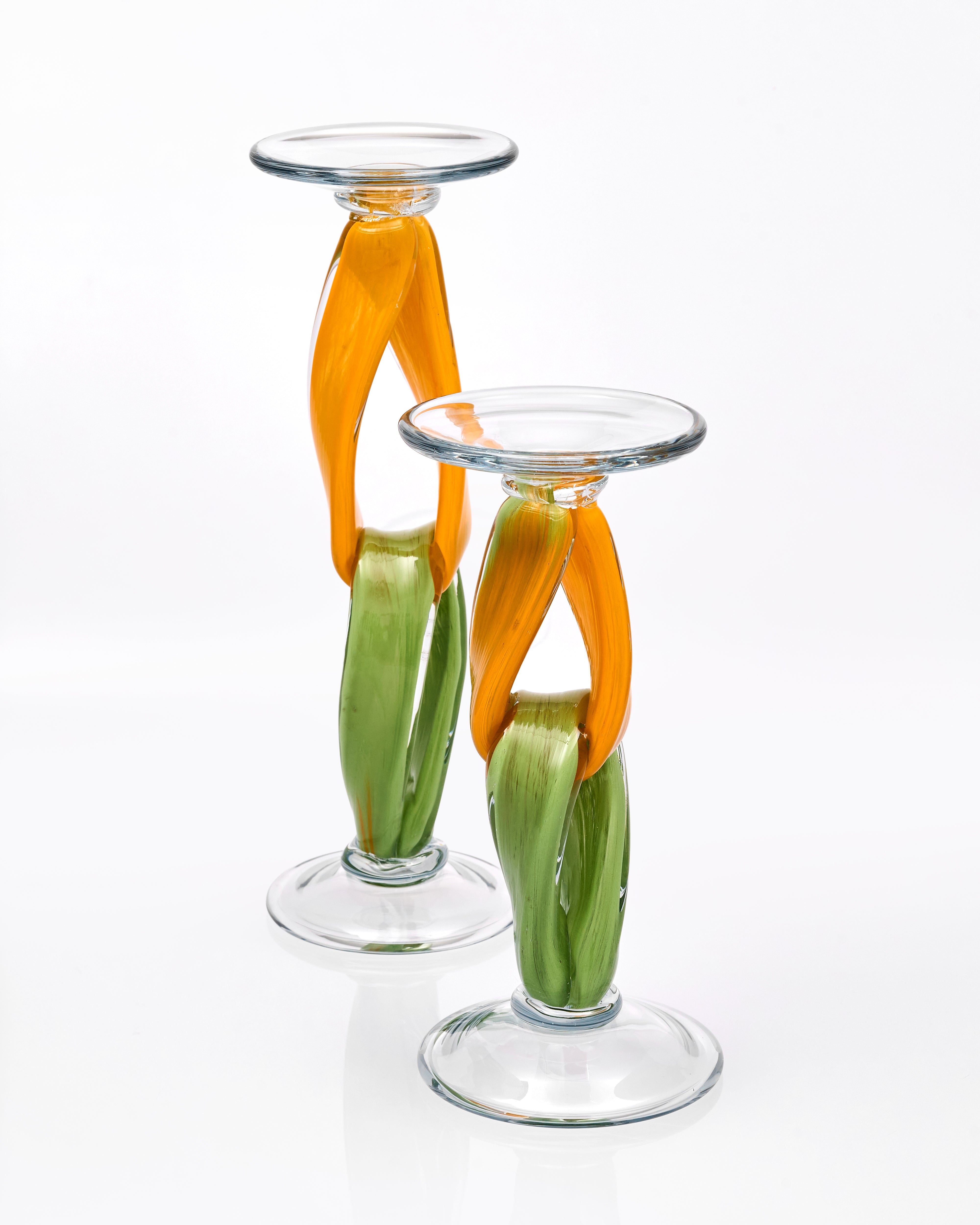 Two glass candle holders with orange and green accents on a white background