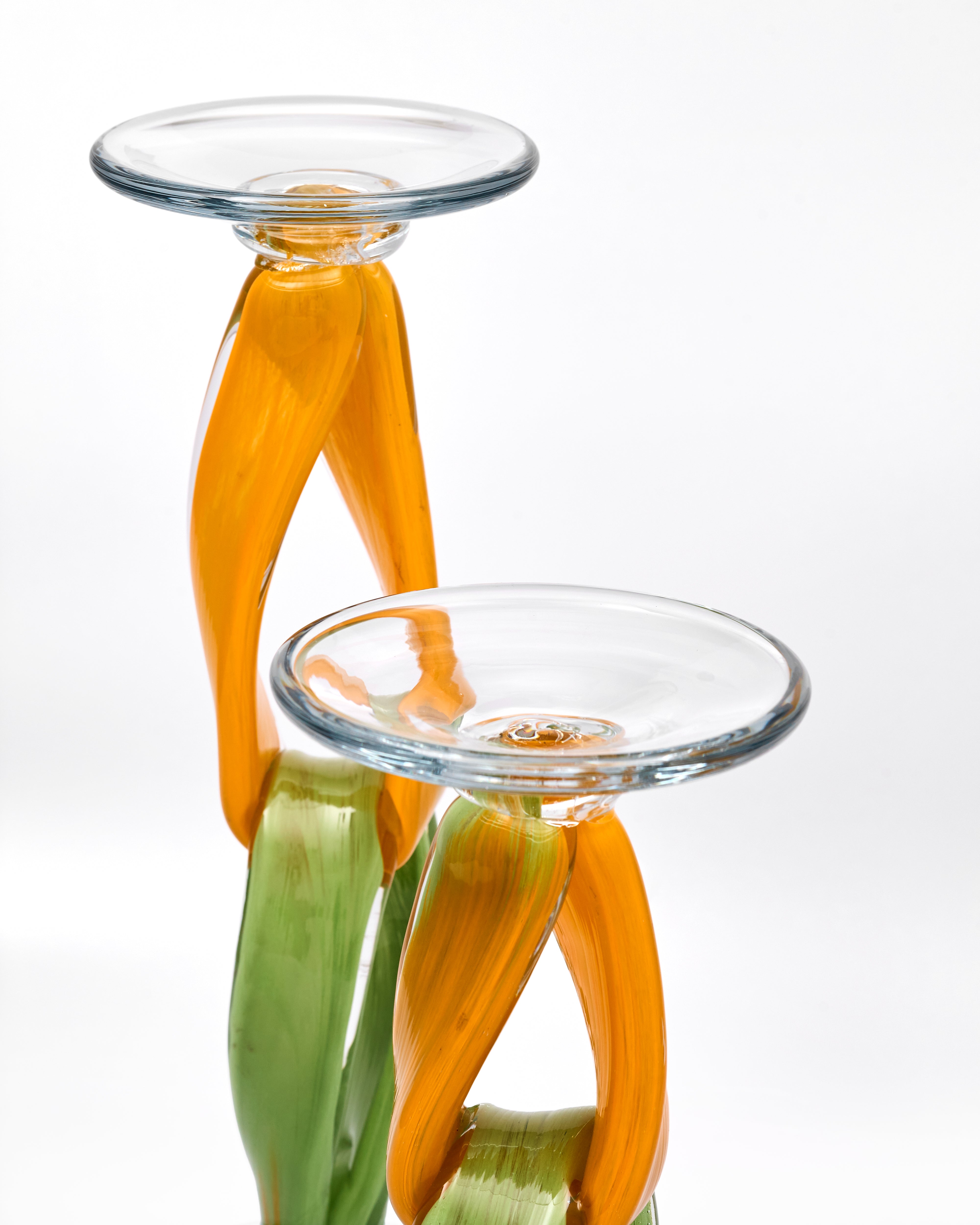 Two glass candle holders with orange and green ribbons on a white background