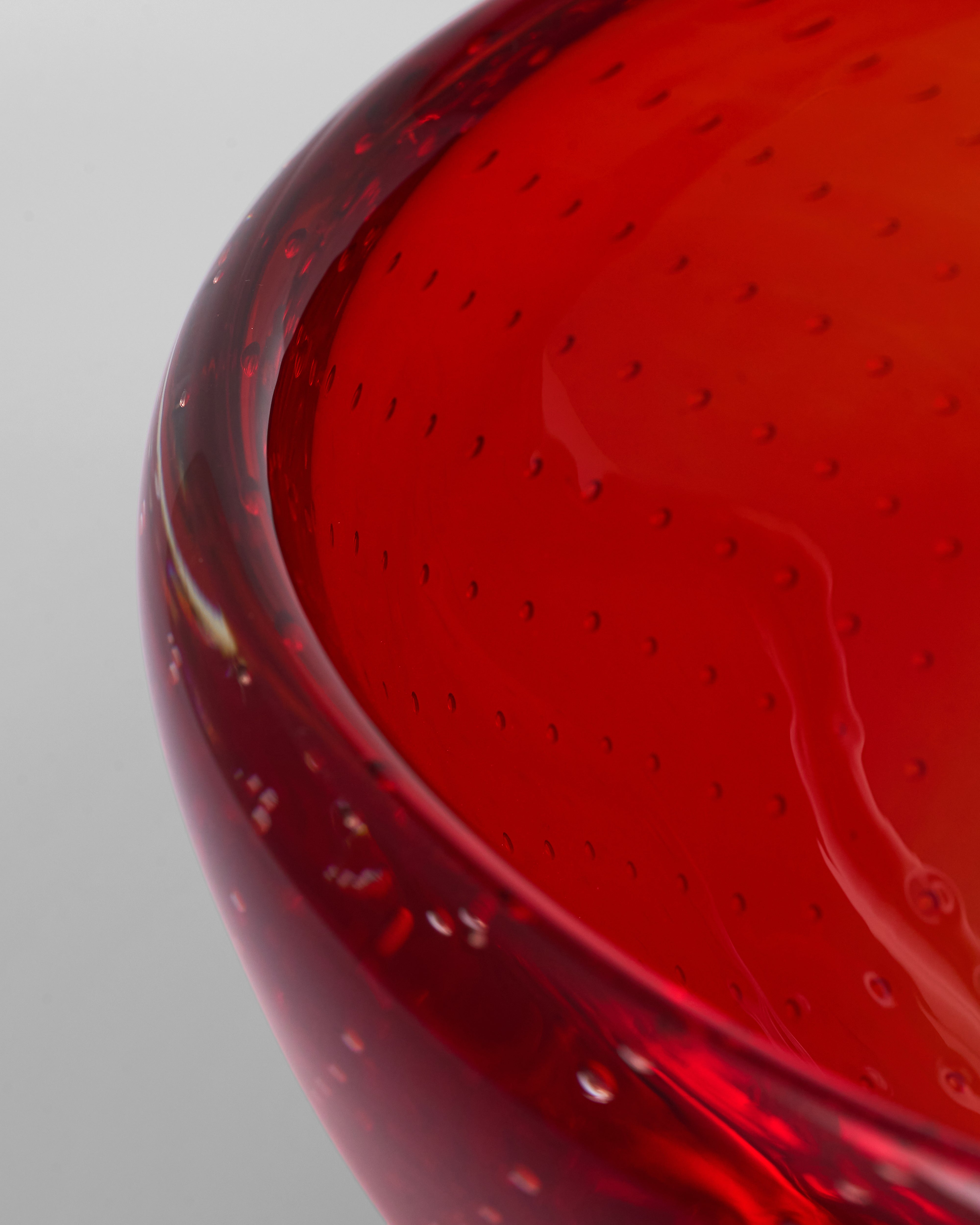 Close-up of a red glass bowl vase with a textured surface on a gray background