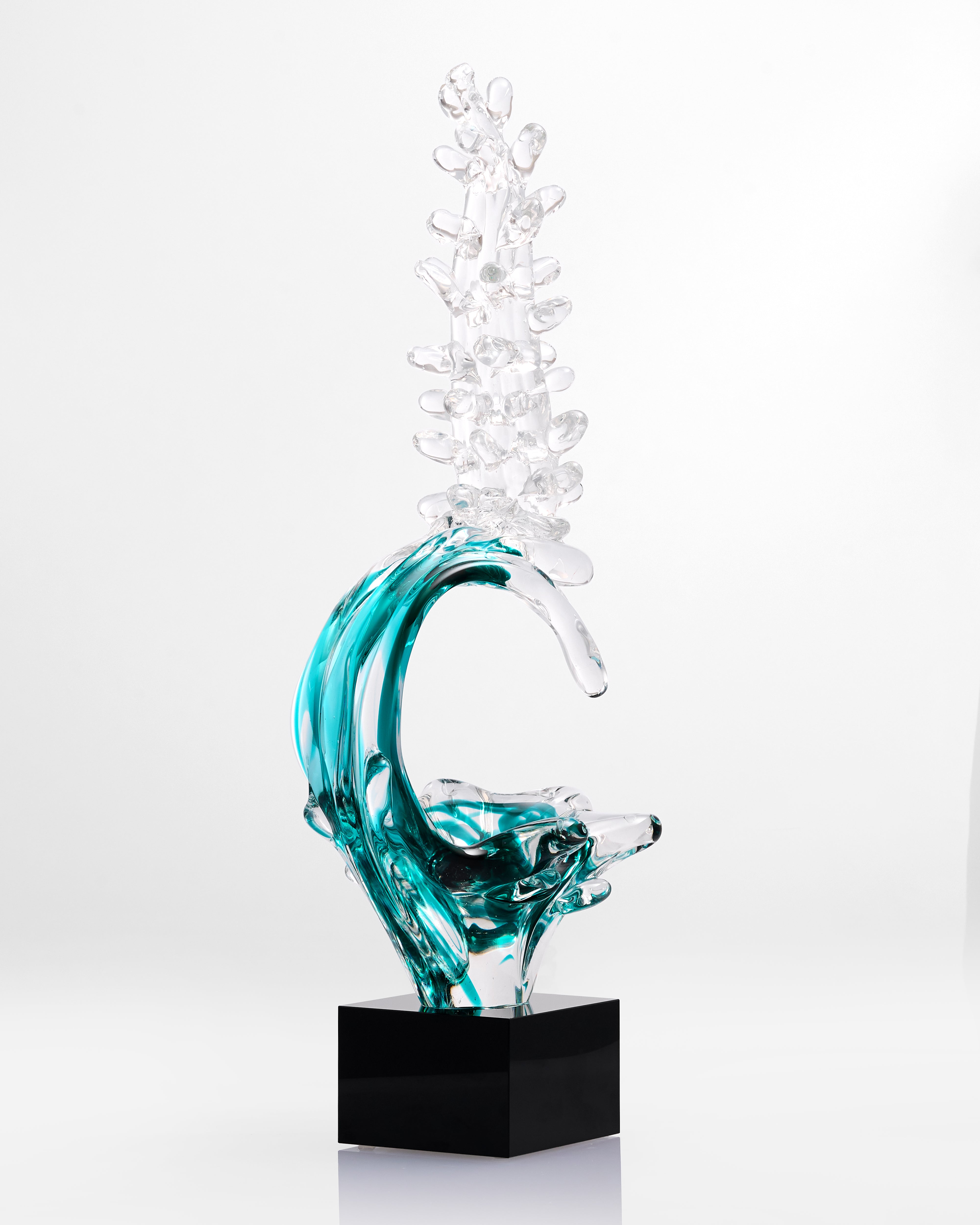 Glass sculpture of a wave with clear and blue colors on a white background