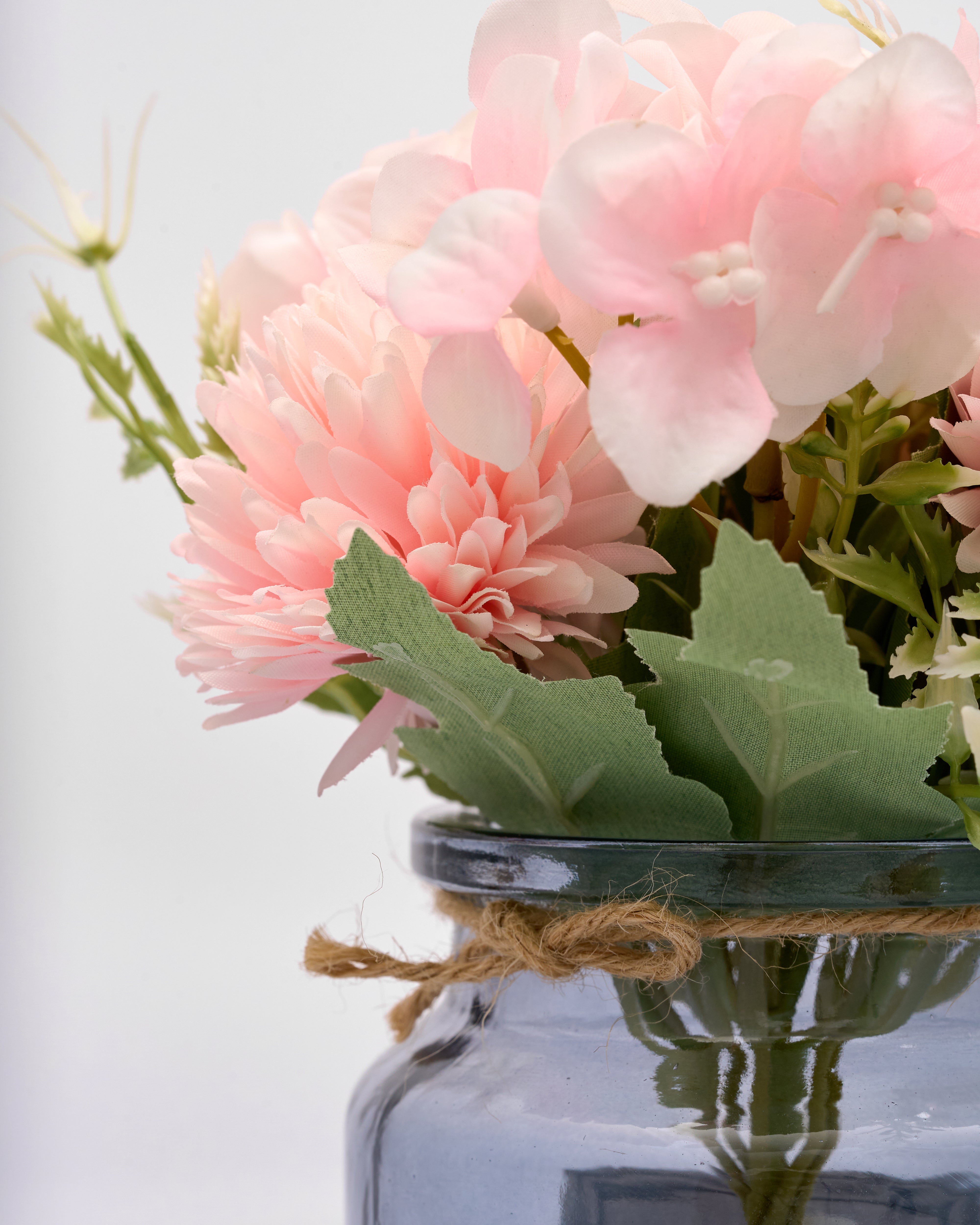Pink flowers in a glass jar with twine on a light background