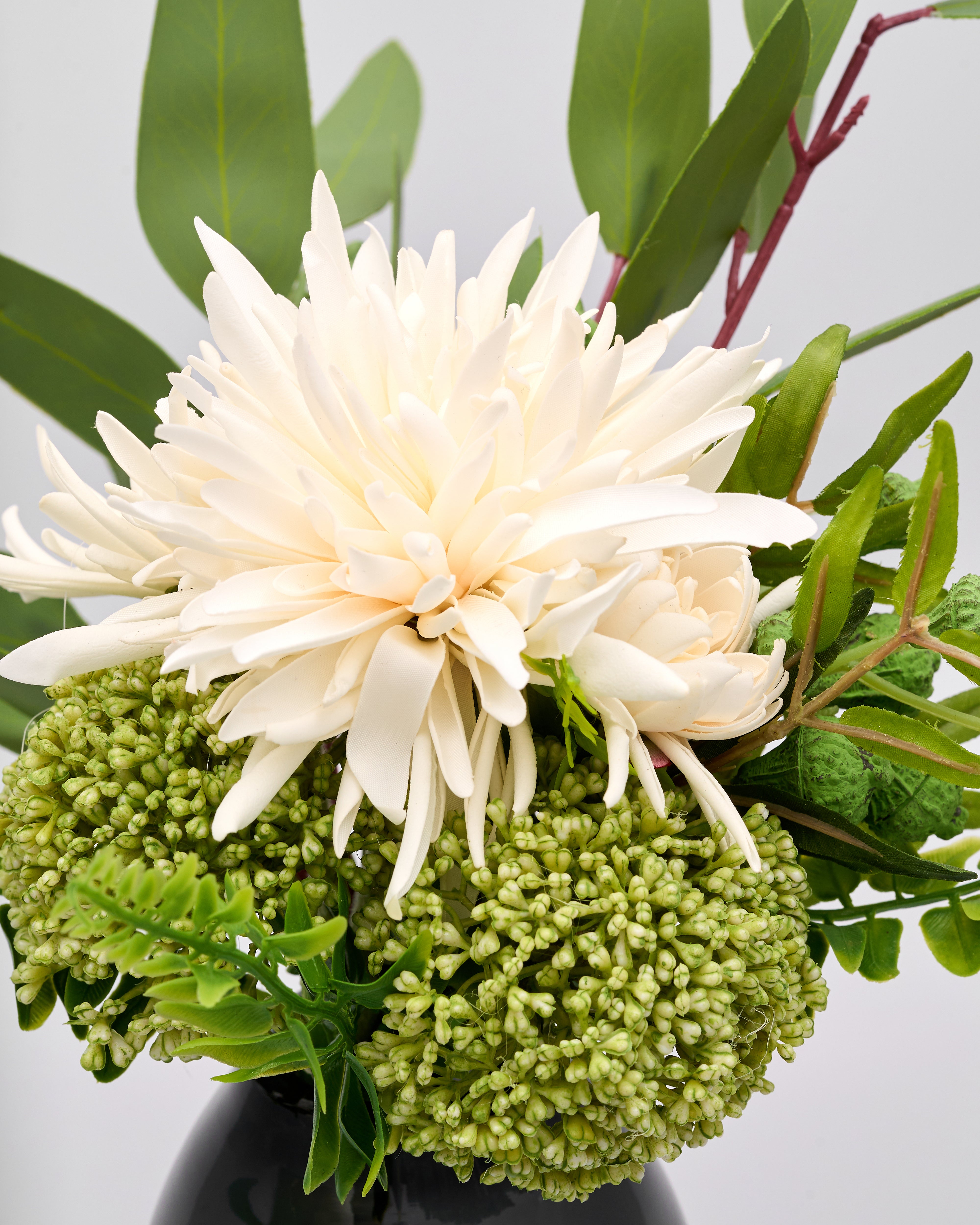 Floral arrangement with a large white flower and green foliage on a light gray background
