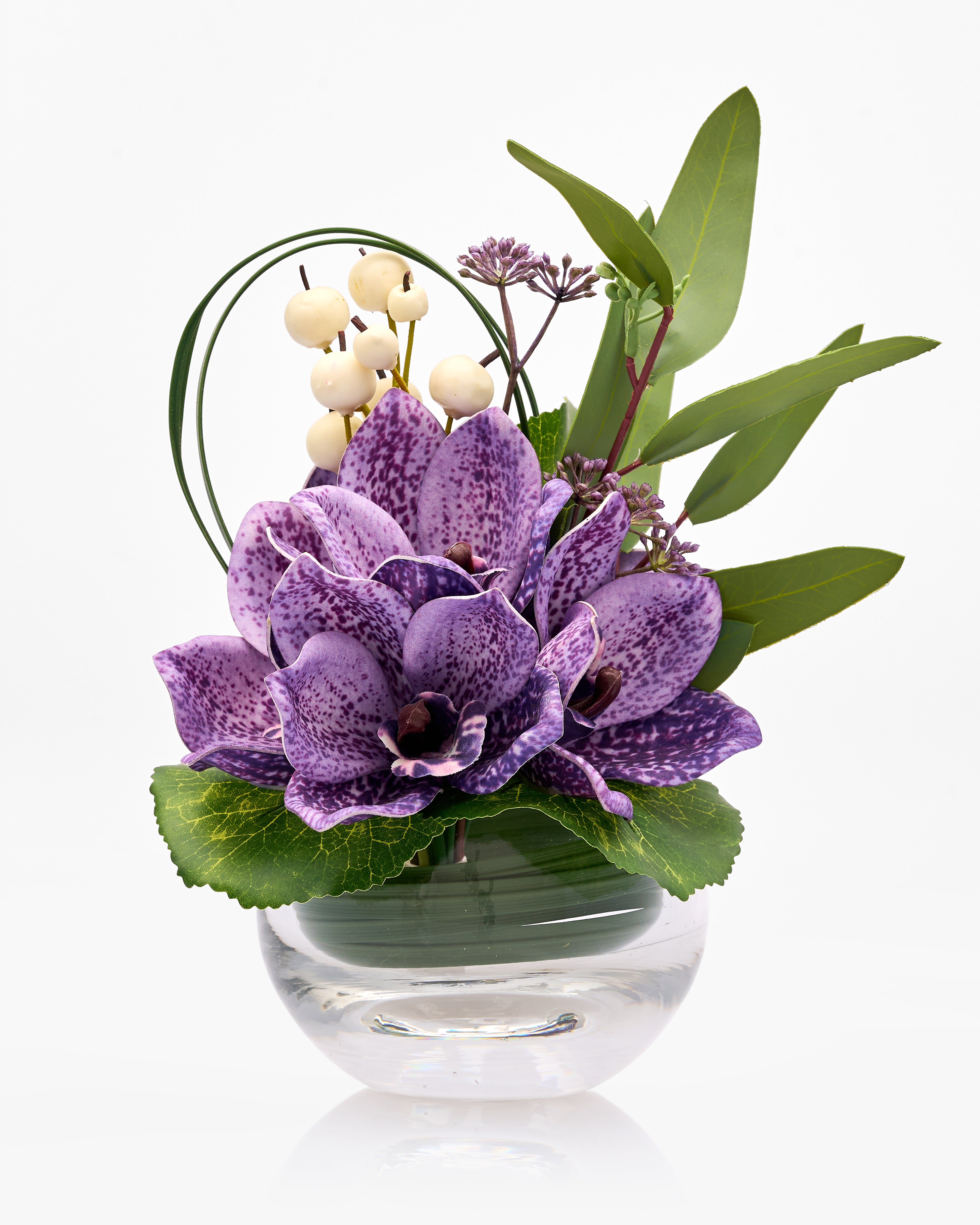Floral arrangement with purple flowers and green leaves in a clear vase on a white background