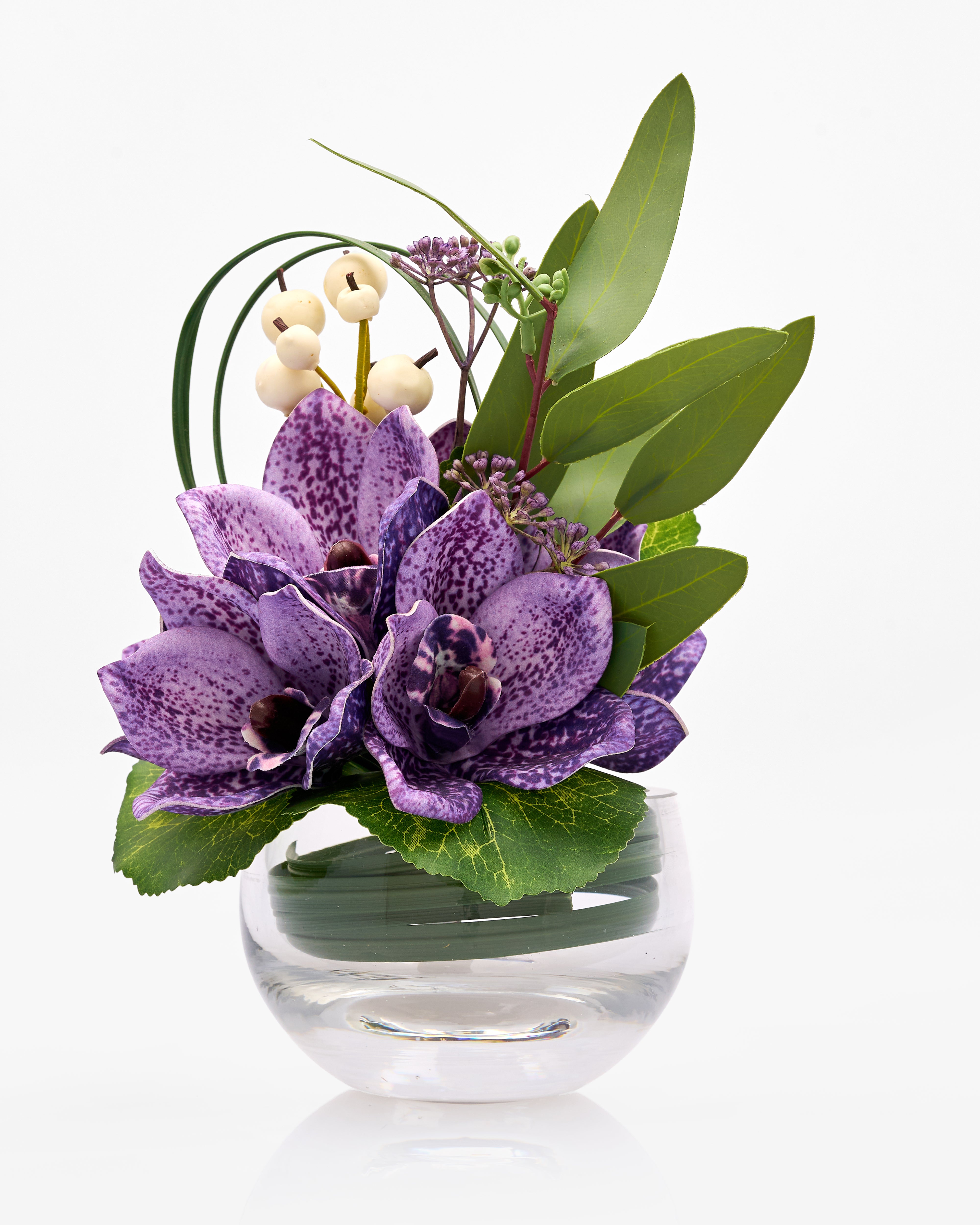 Floral arrangement with purple flowers and green leaves in a clear glass vase on a white background